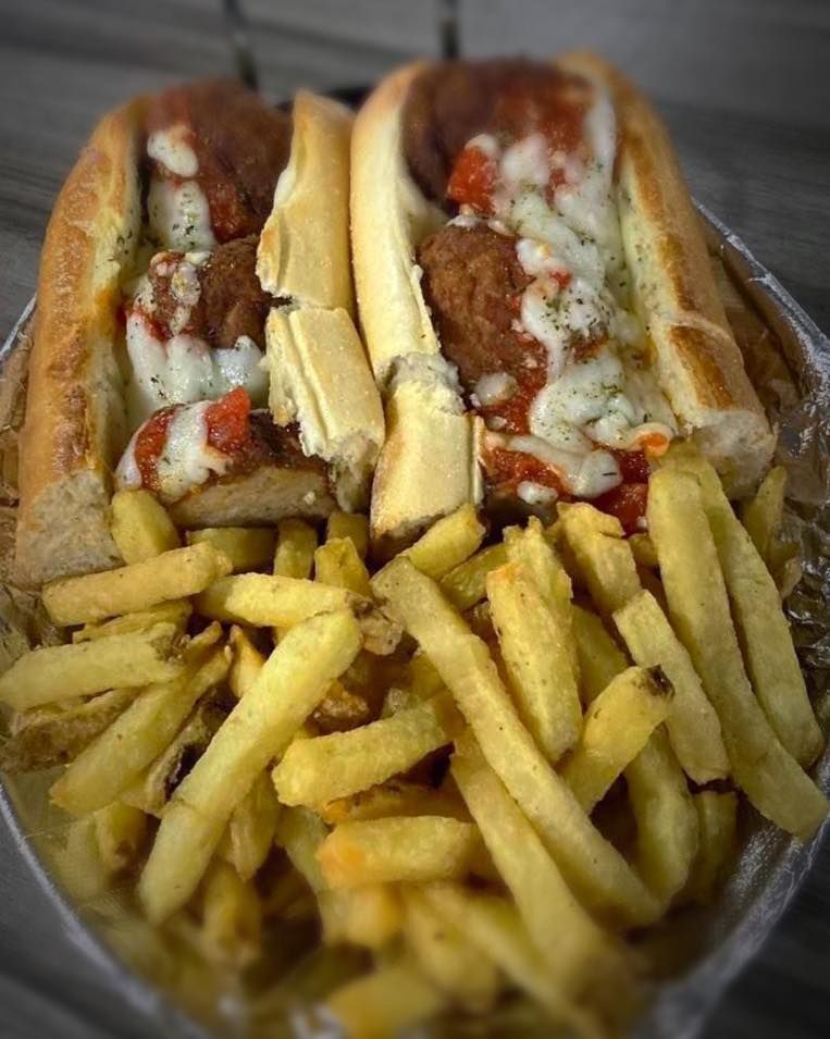 A meatball sub sandwich with french fries in a plastic container.