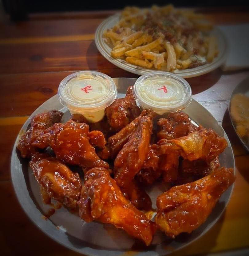 A plate of chicken wings with two dipping sauces next to a plate of french fries