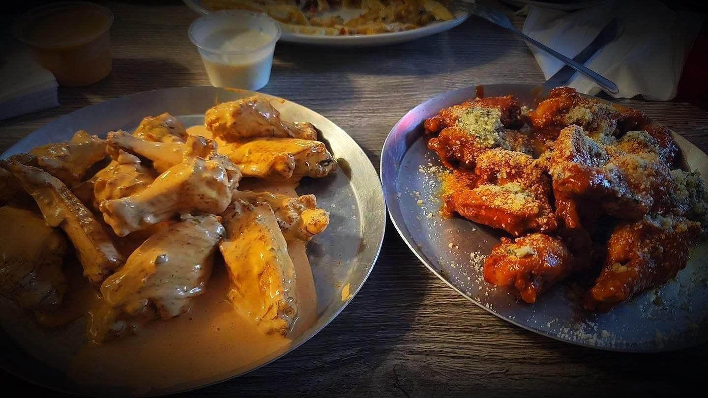 Two plates of chicken wings are sitting on a wooden table.