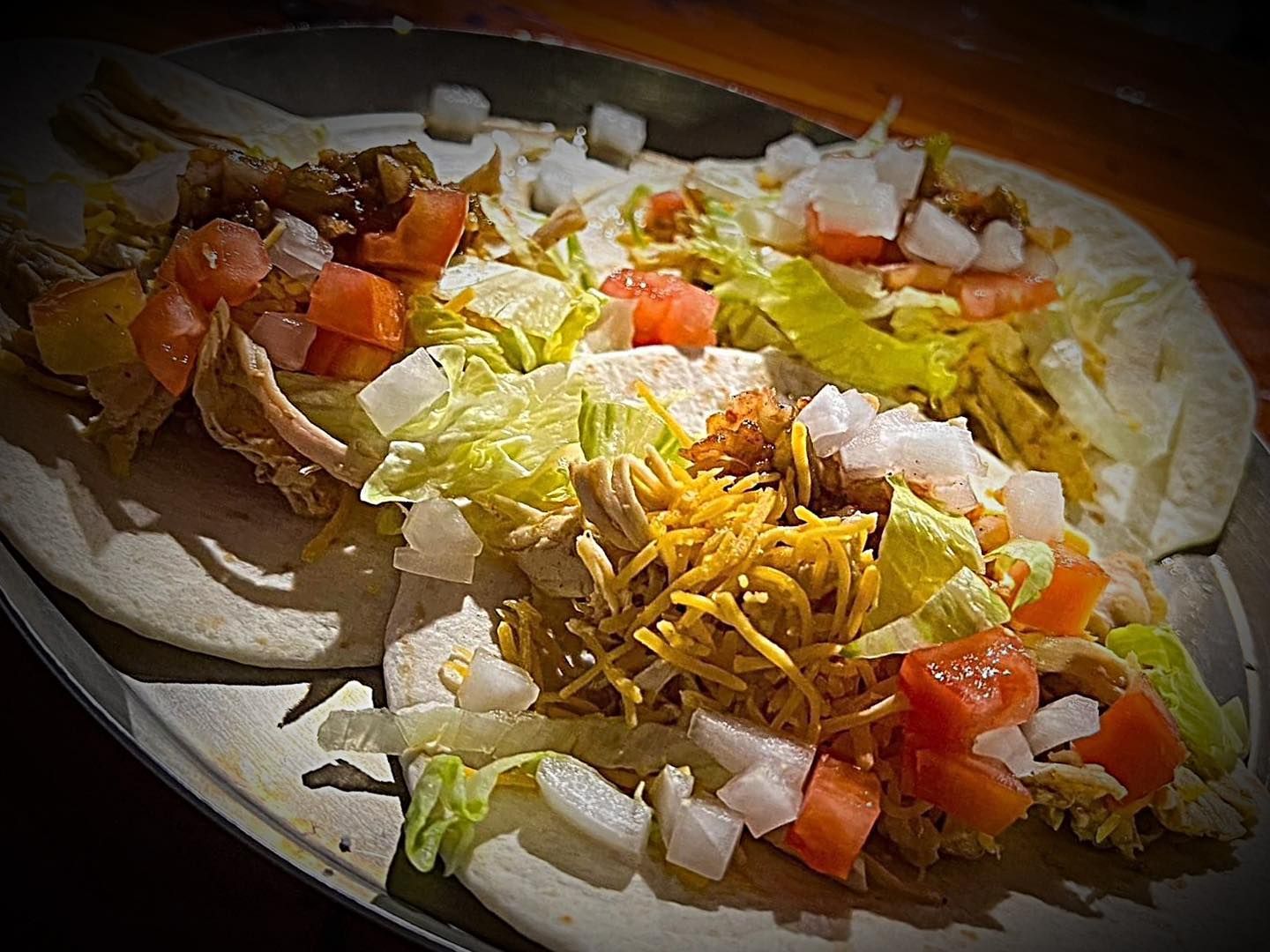 A close up of a taco with lettuce , tomatoes , onions and cheese on a plate.
