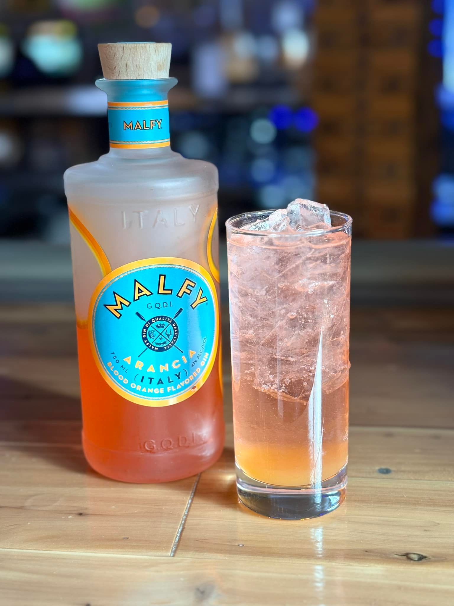 A bottle of bala gin next to a glass of it on a wooden table.