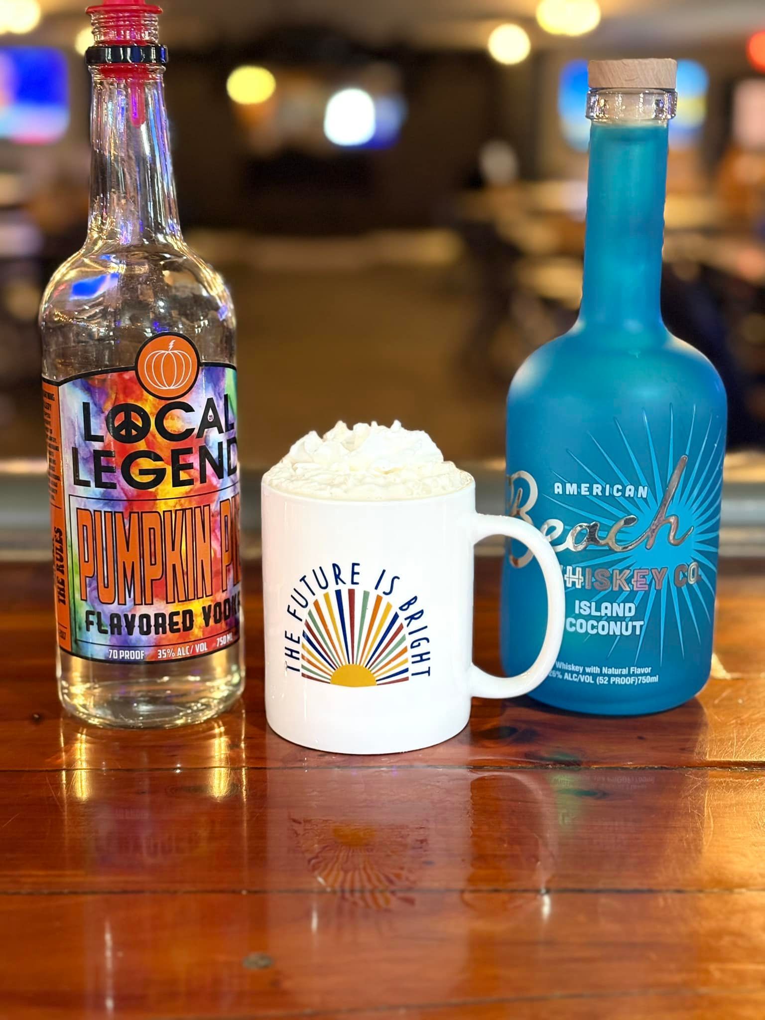 Two bottles of alcohol and a mug with whipped cream on a wooden table.