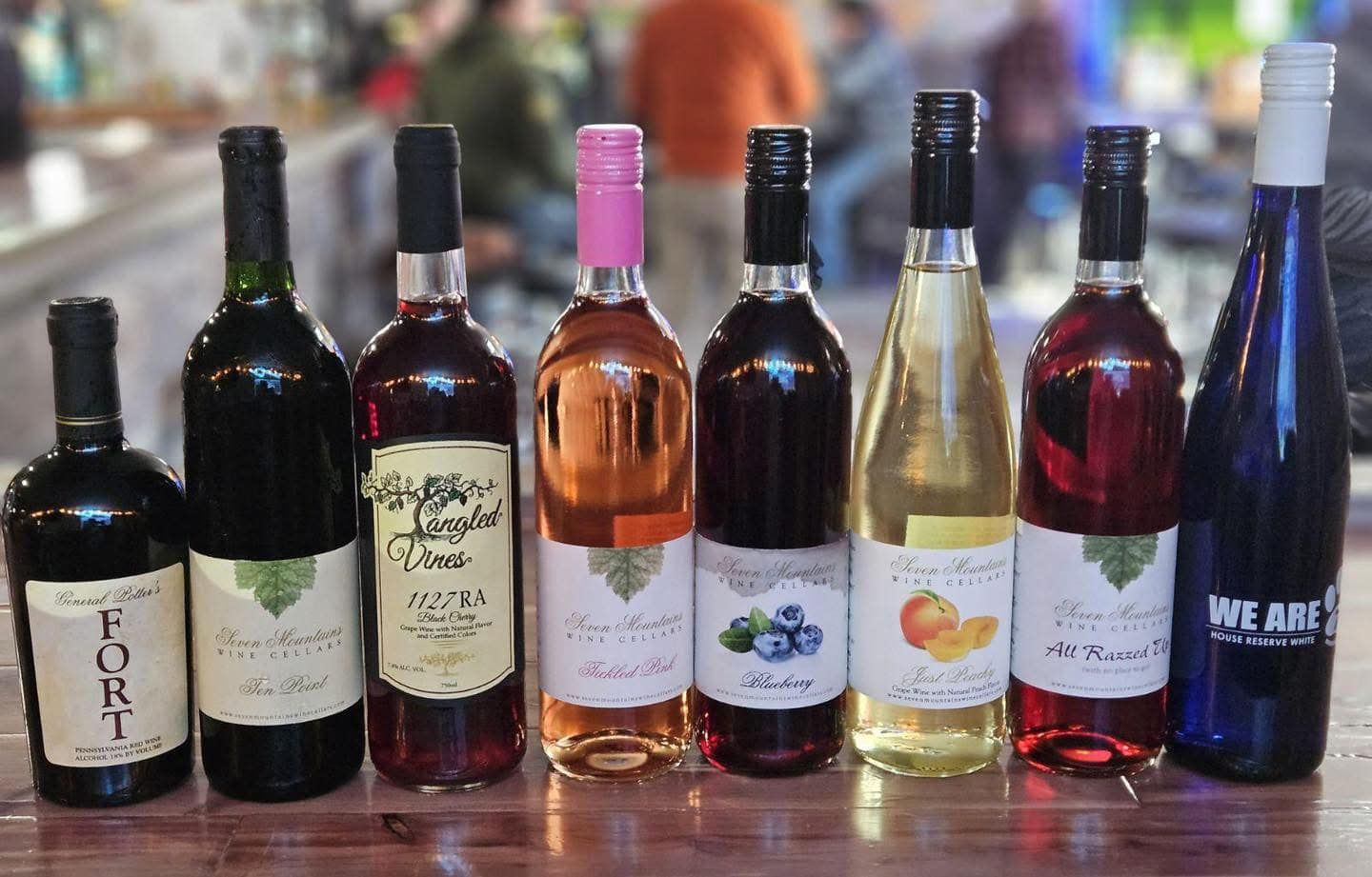 A row of wine bottles are lined up on a wooden table.