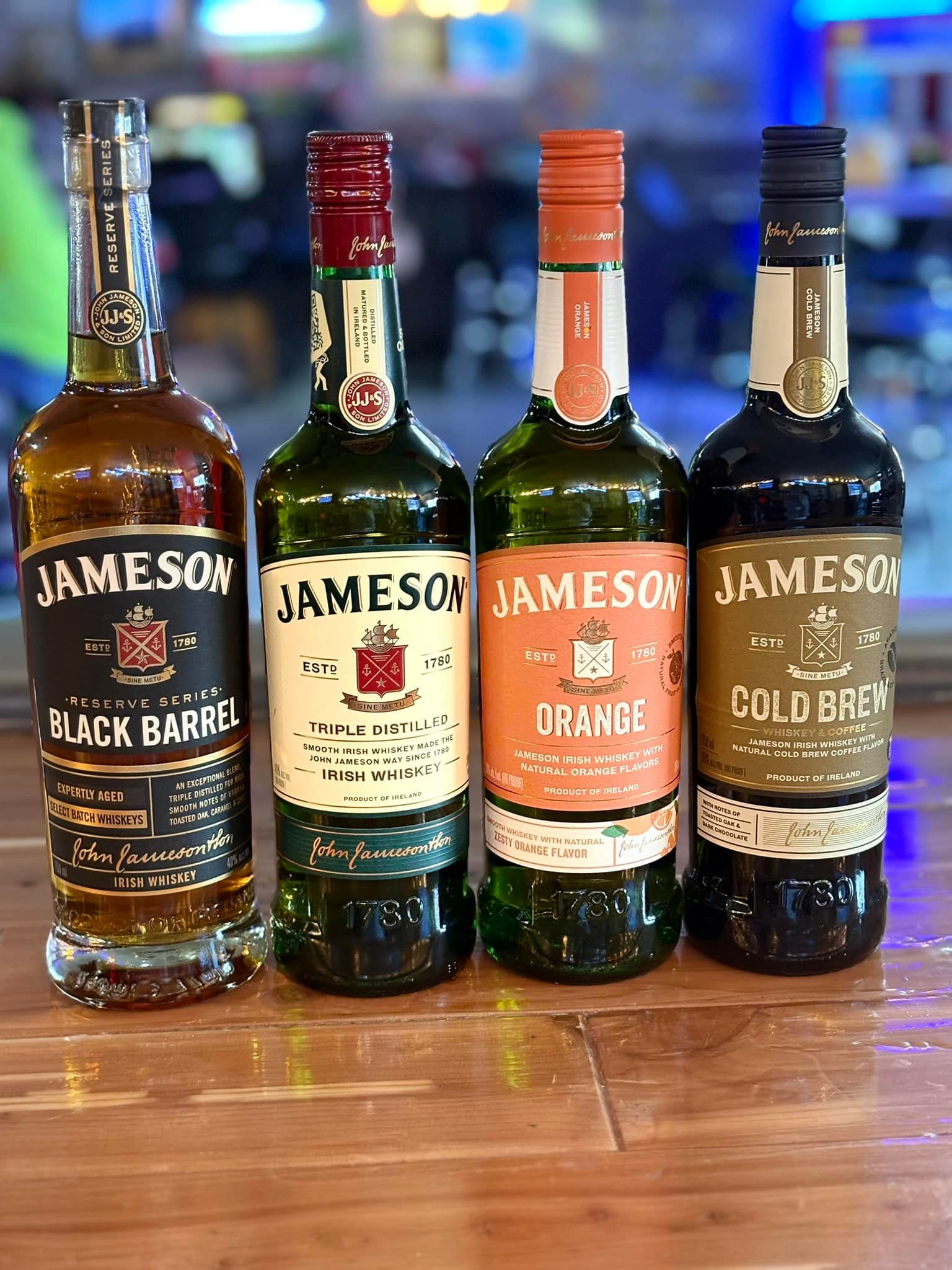 Four bottles of jameson whiskey are sitting on a wooden table.