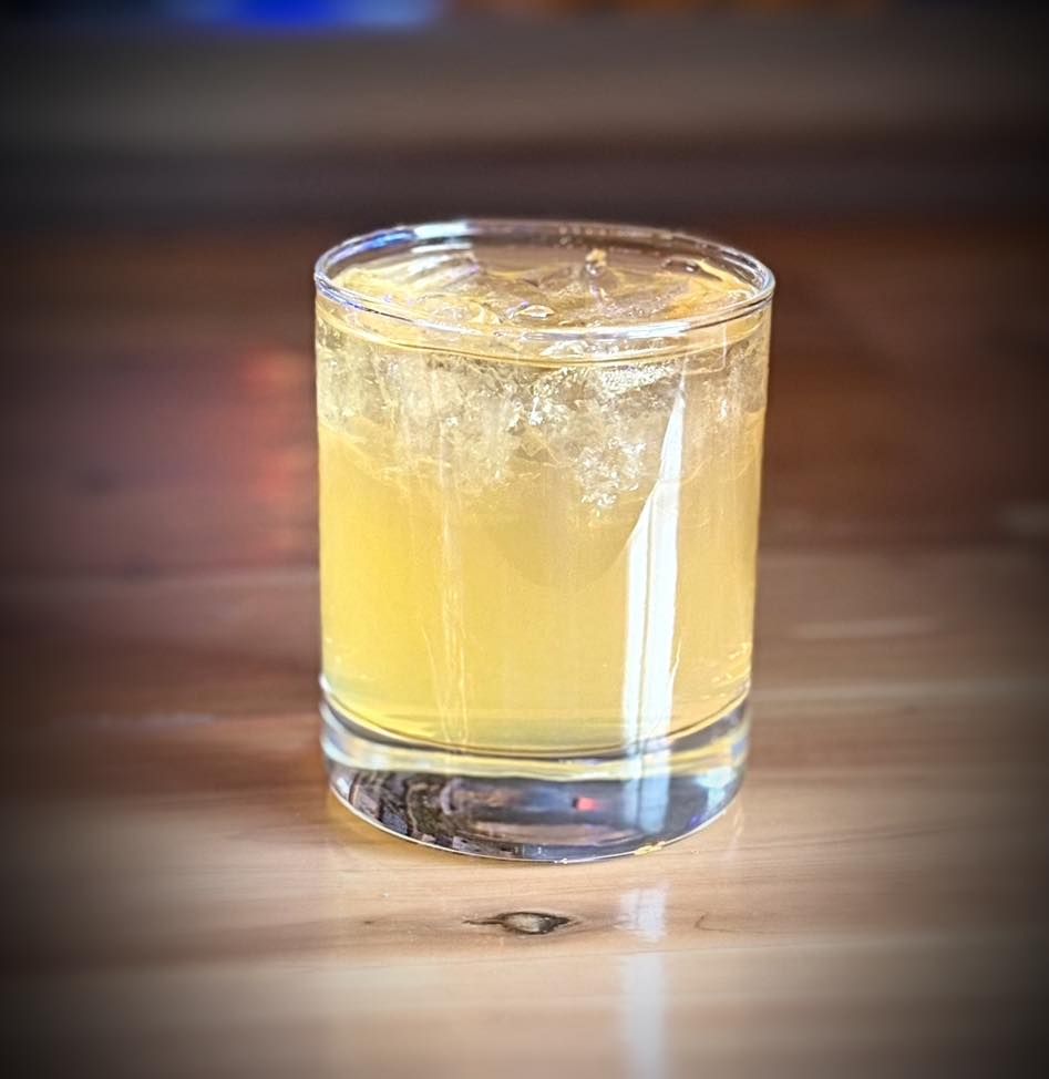 A glass of yellow liquid is sitting on a wooden table.