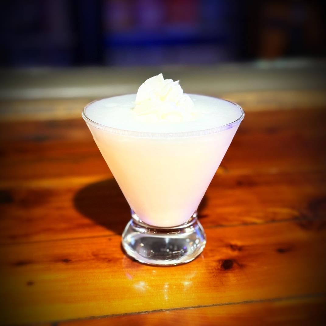 A martini with whipped cream on top is on a wooden table