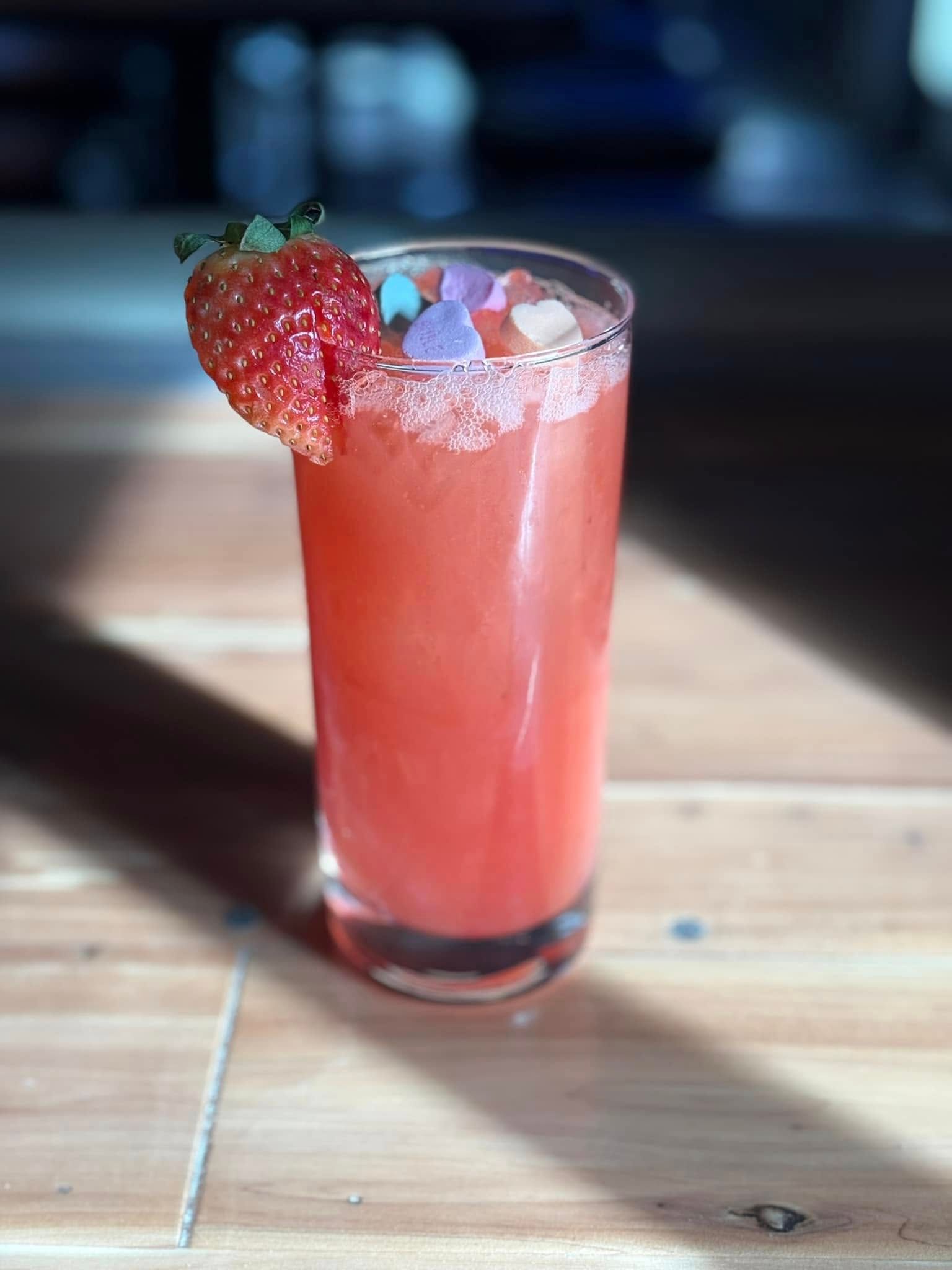 A glass of pink liquid with a strawberry on top on a wooden table.