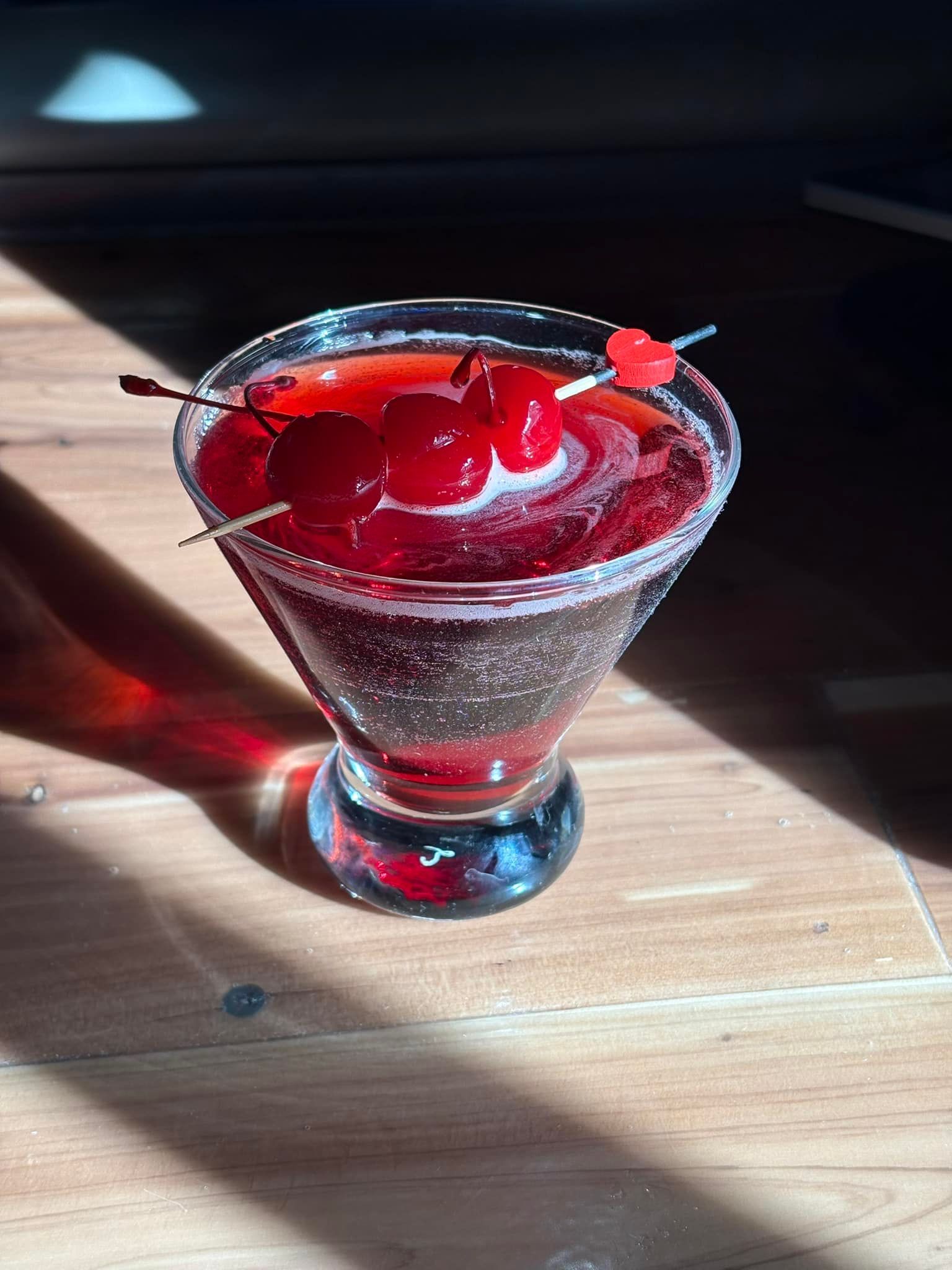 A martini with a cherry on top is on a wooden table.