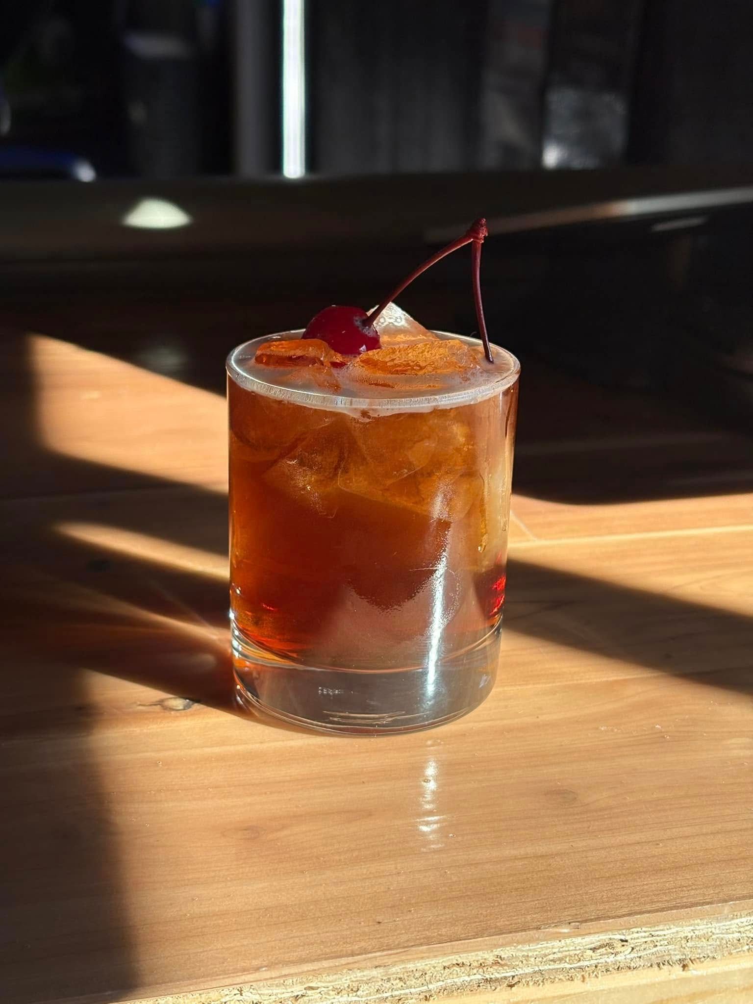 A close up of a drink with a cherry on top on a wooden table.