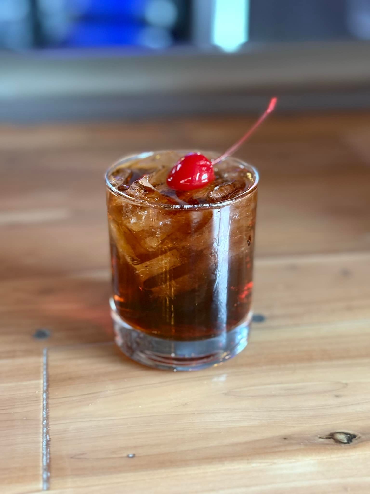 A close up of a drink with a cherry on top on a wooden table.