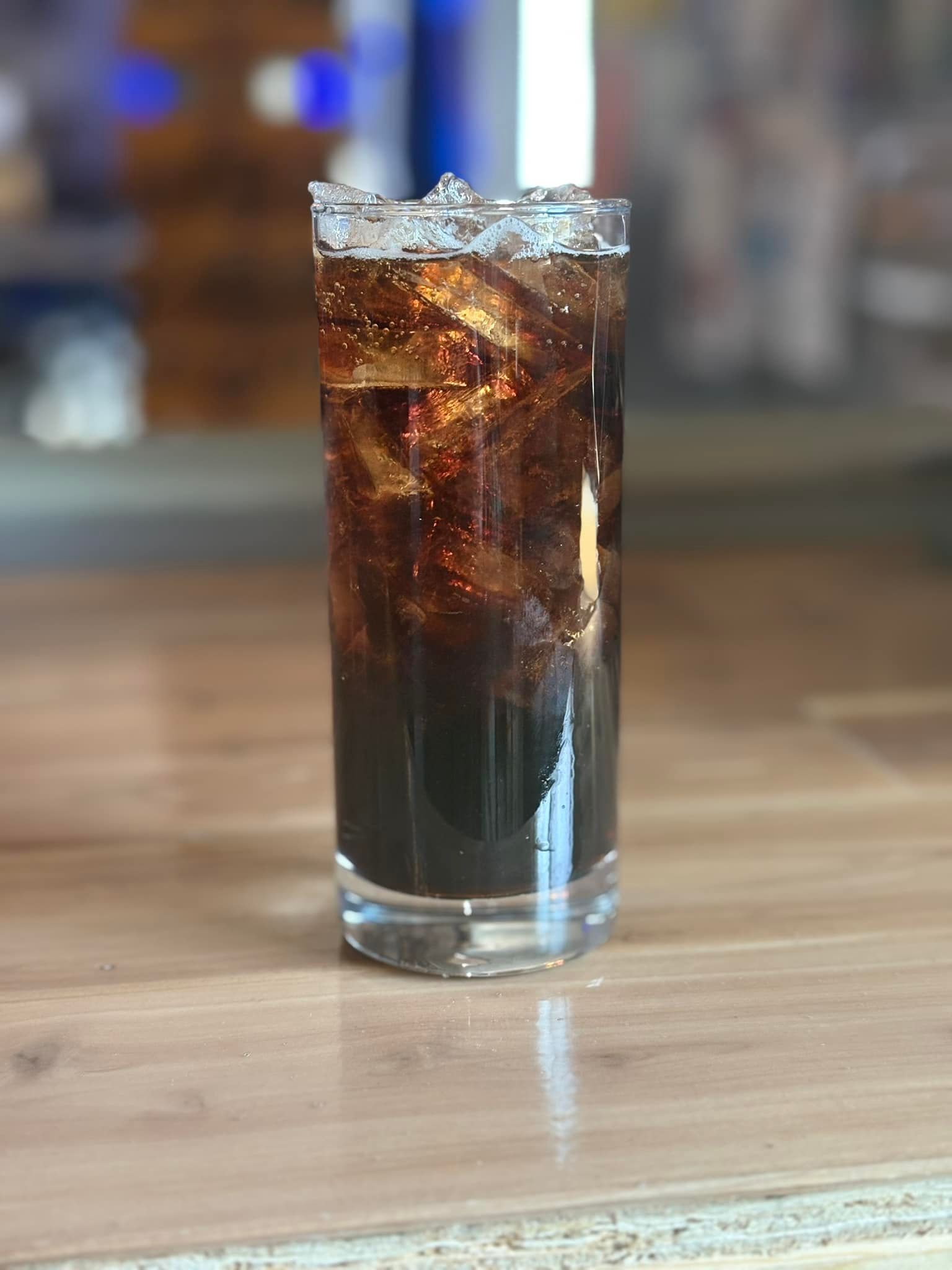 A glass of cola with ice is sitting on a wooden table.