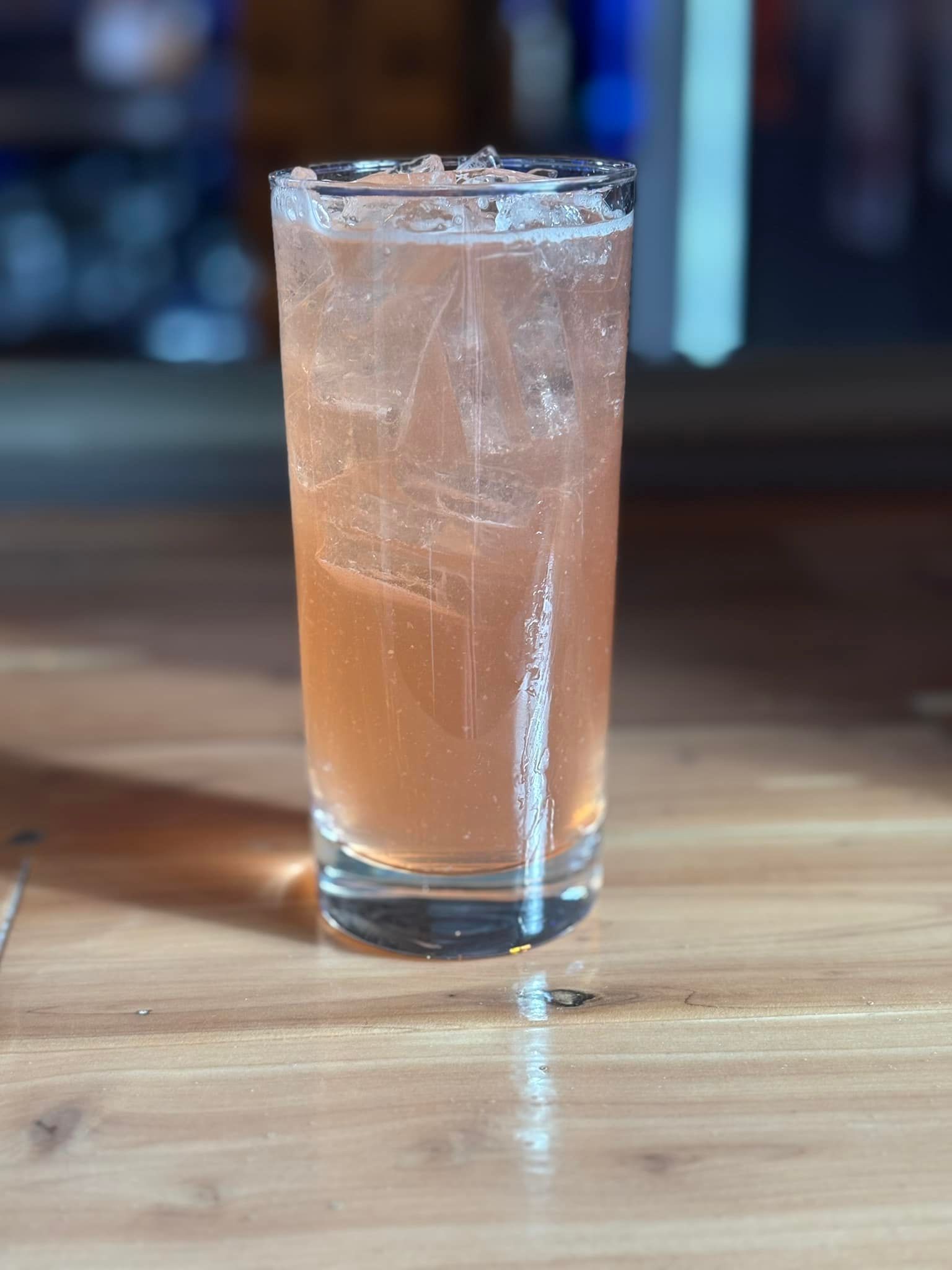 A tall glass filled with a pink liquid is sitting on a wooden table.