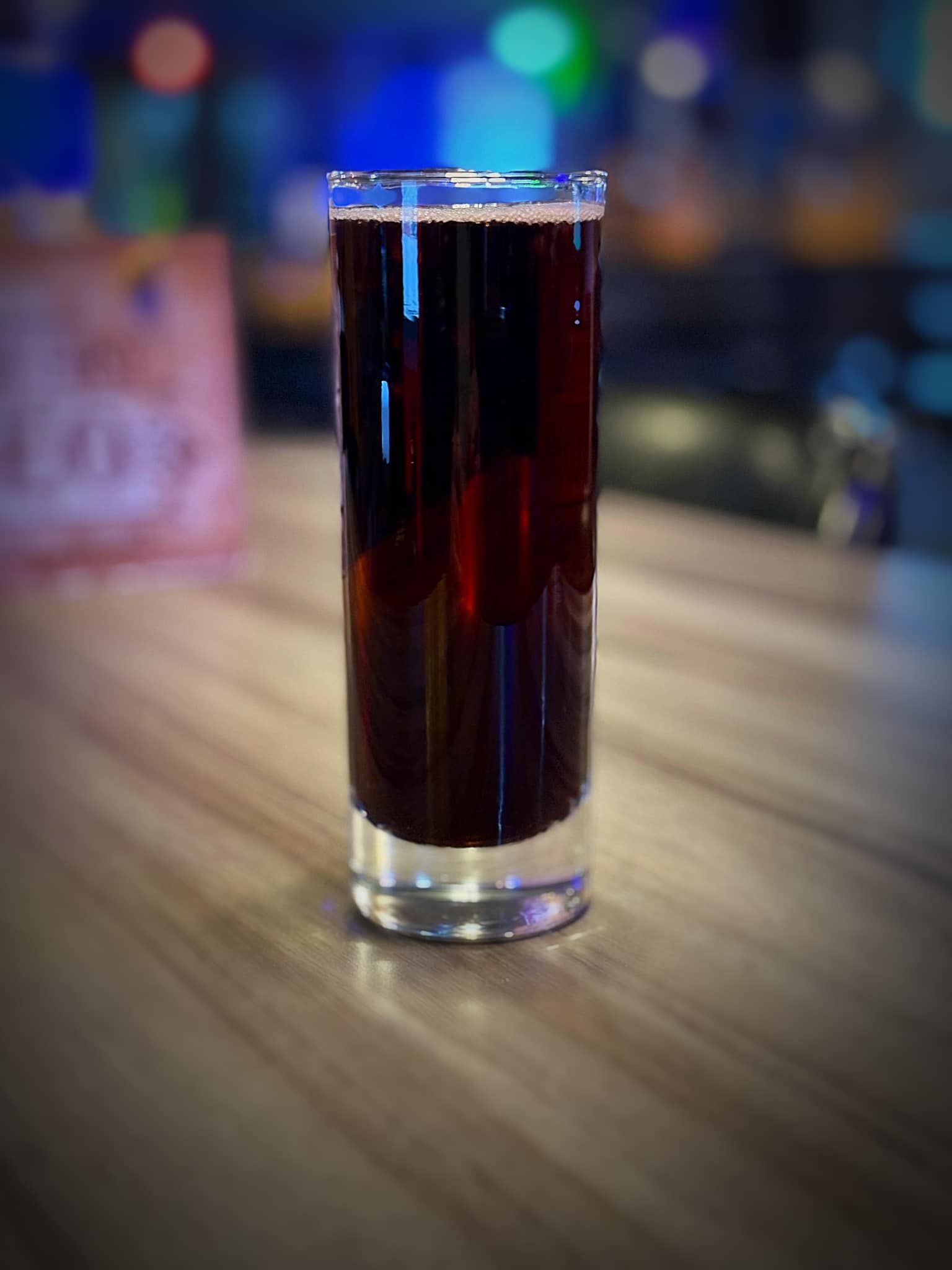 A tall glass of beer is sitting on a wooden table.