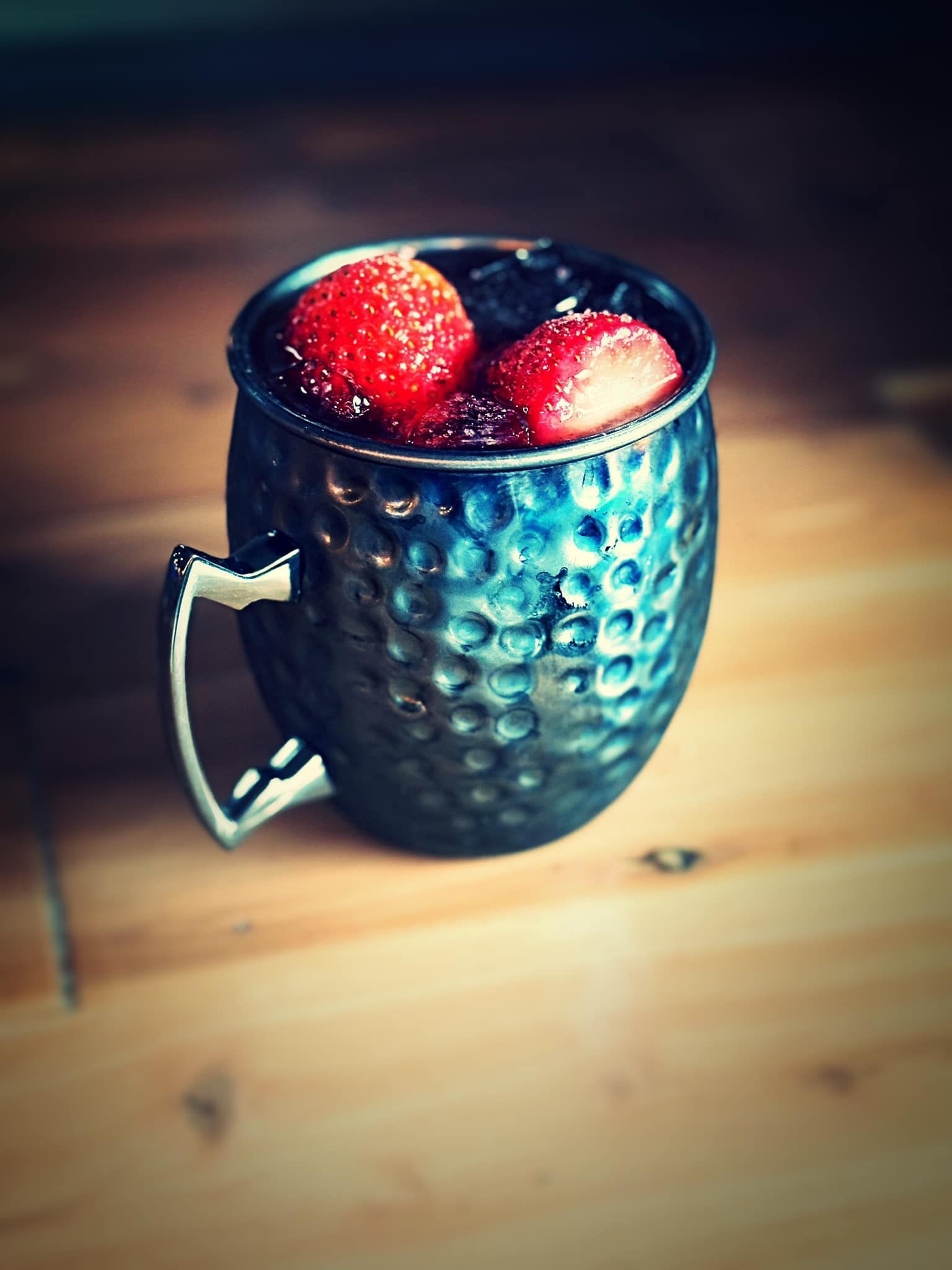A blue mug filled with strawberries on a wooden table