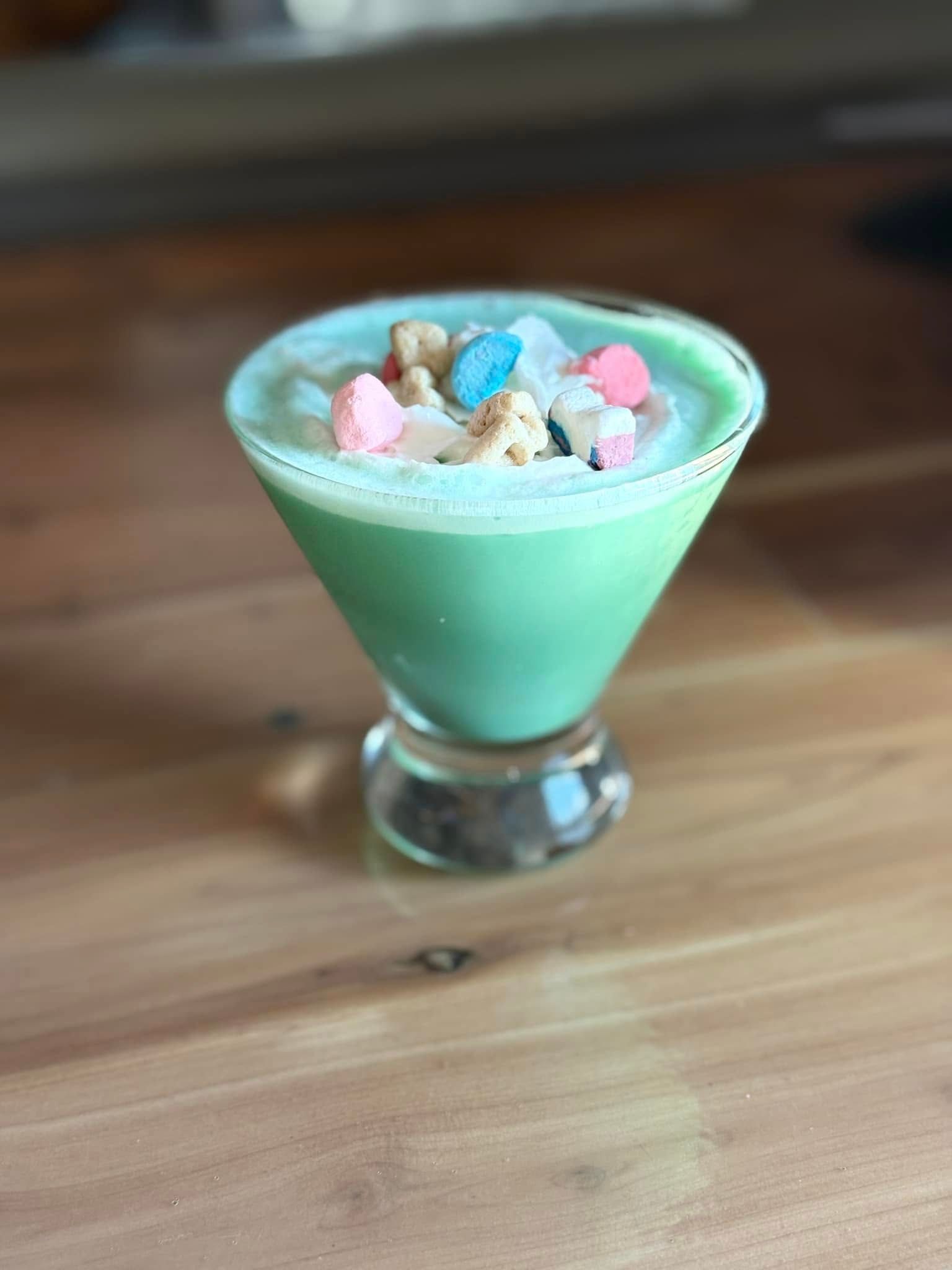 A green drink in a martini glass on a wooden table.