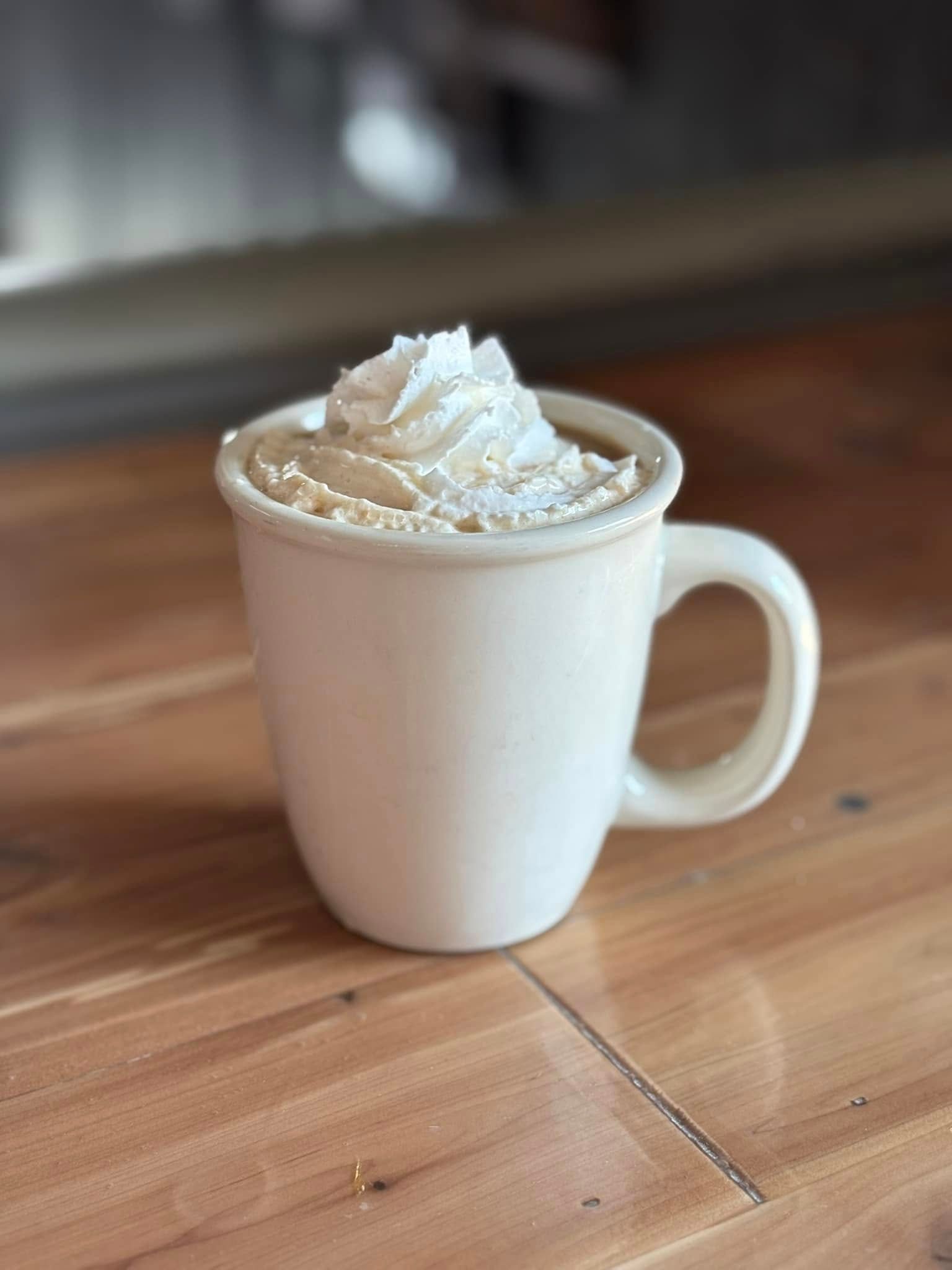 A cup of coffee with whipped cream on top is on a wooden table.
