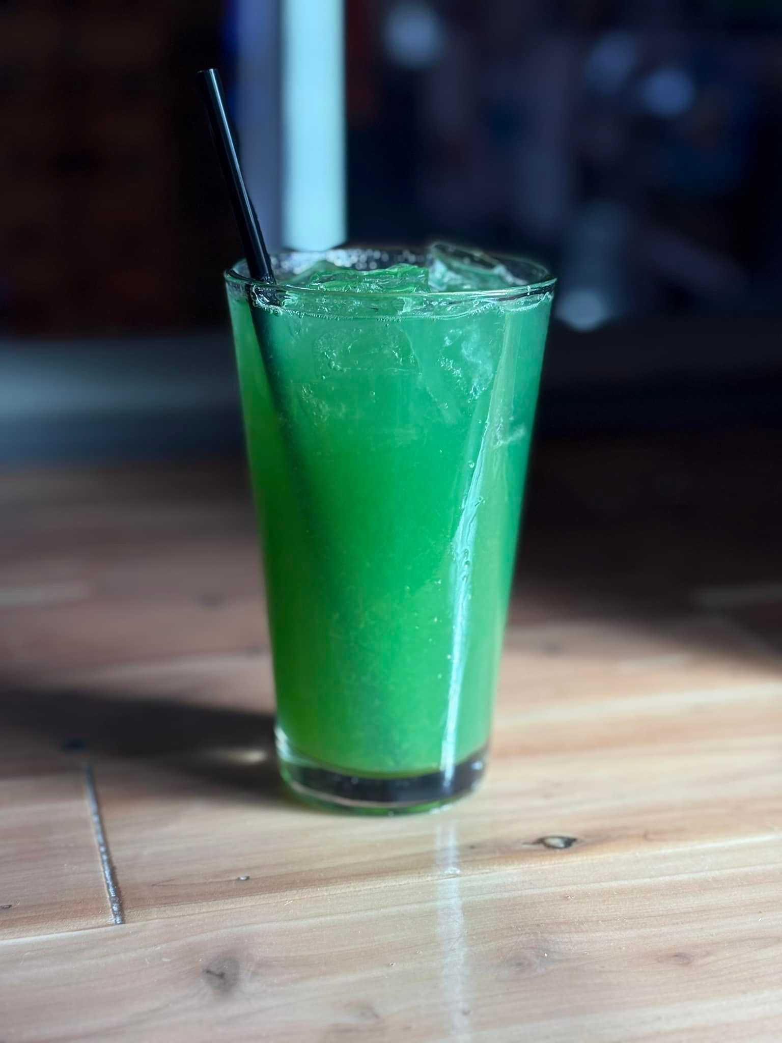 A green drink in a tall glass with a straw on a wooden table.
