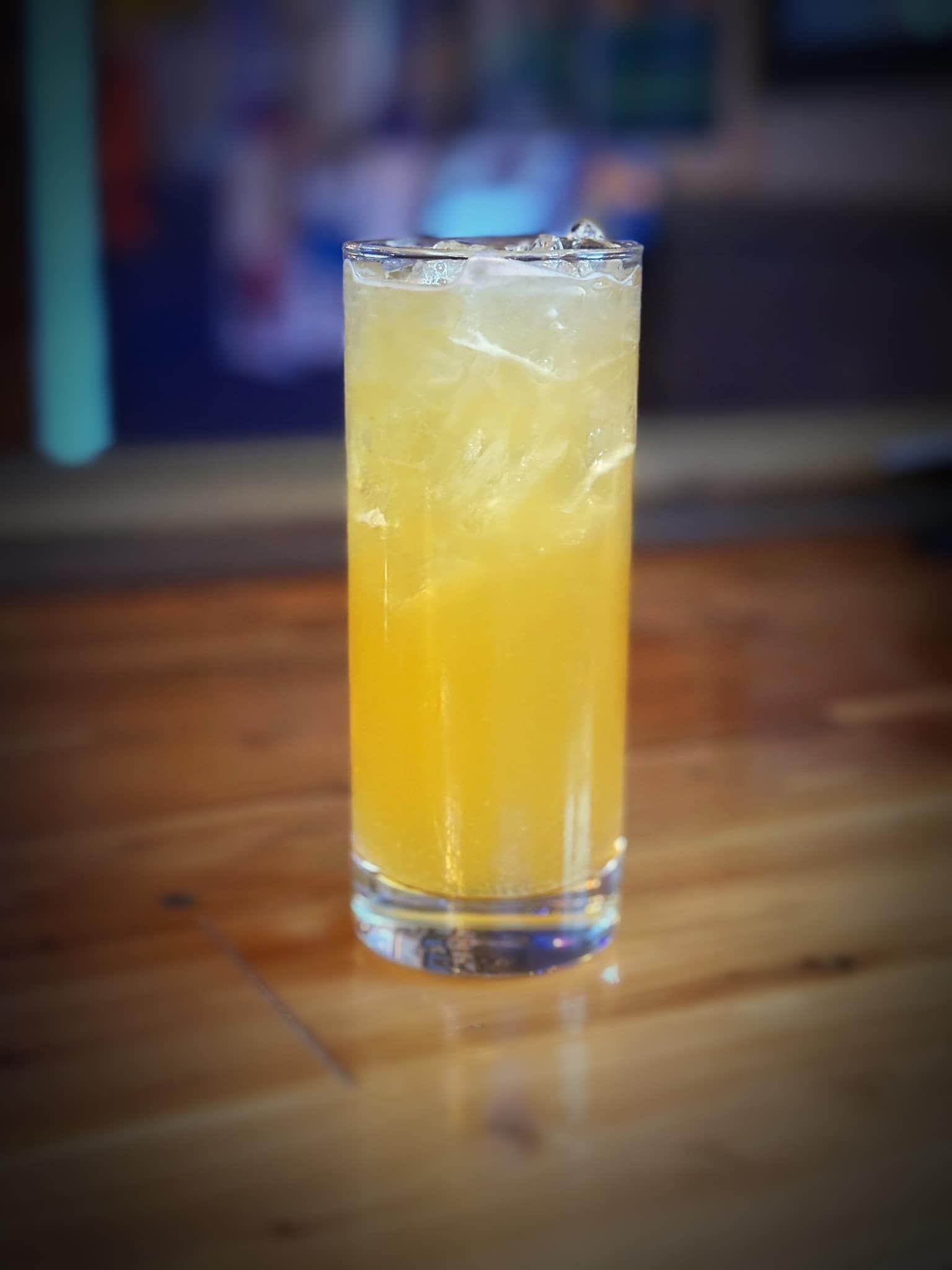 A tall glass filled with a yellow liquid is sitting on a wooden table.