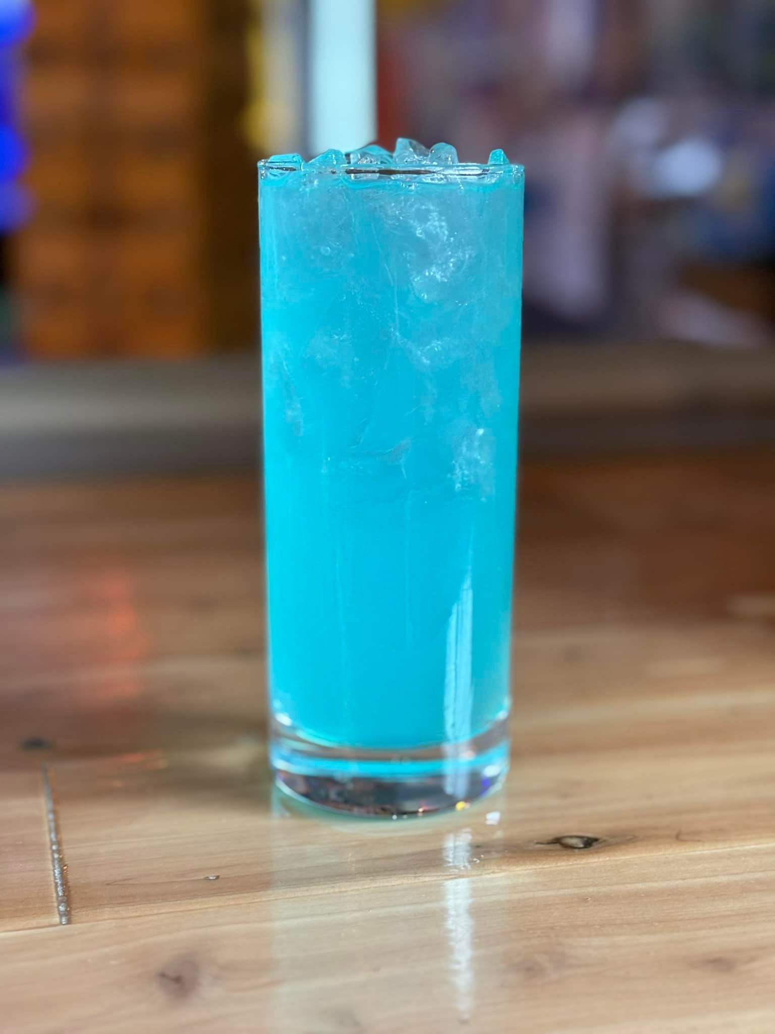 A blue drink in a tall glass on a wooden table.