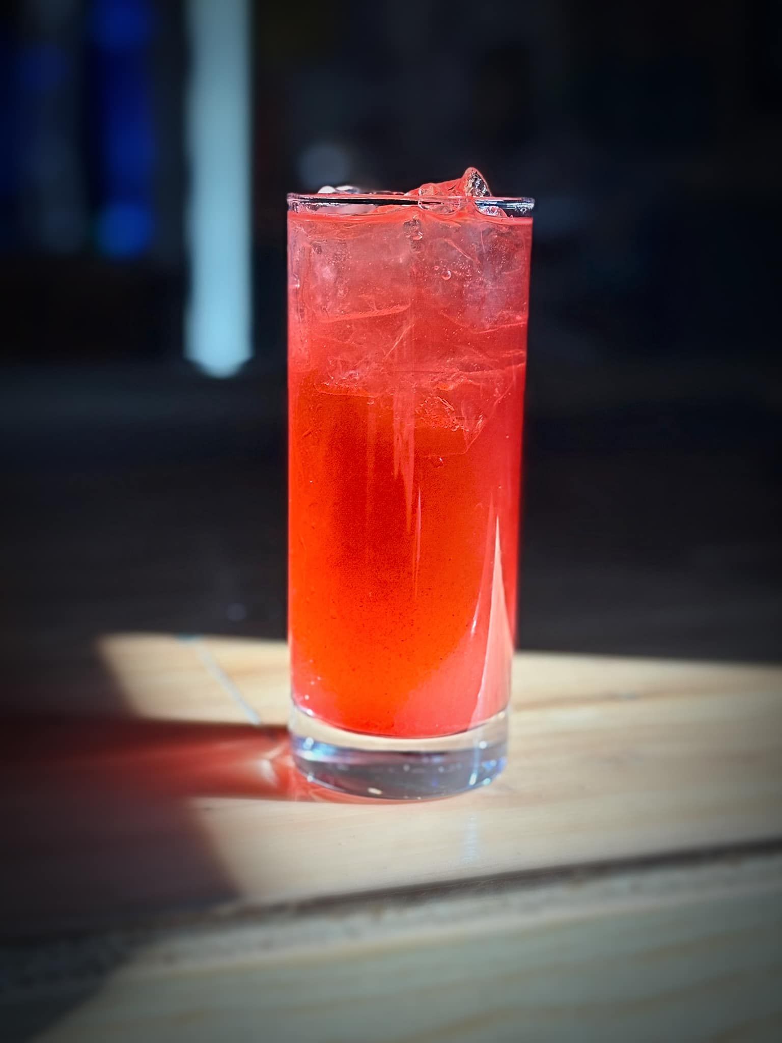 A glass of red liquid is sitting on a wooden table.