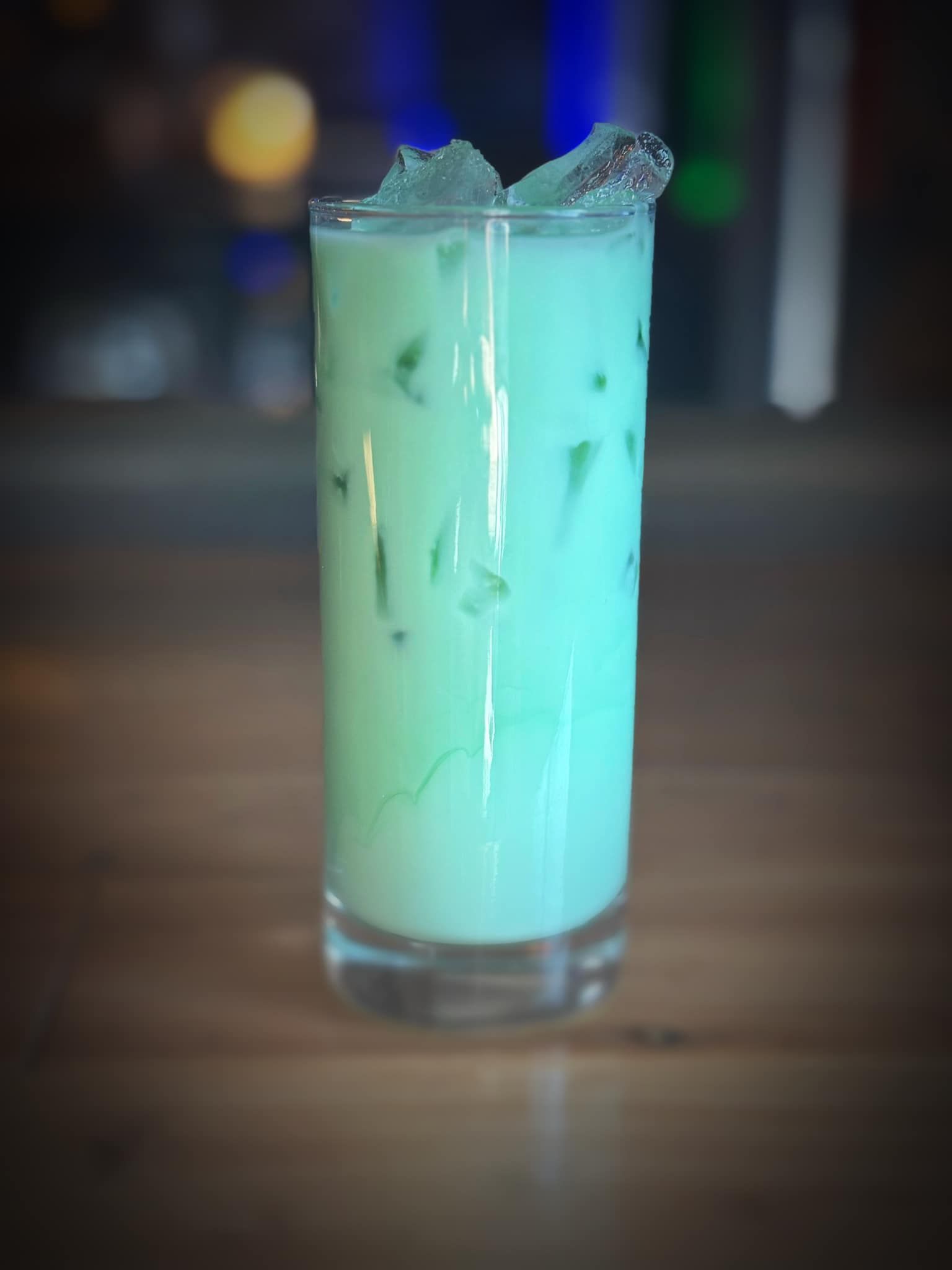 A tall glass filled with a green liquid and ice on a wooden table.