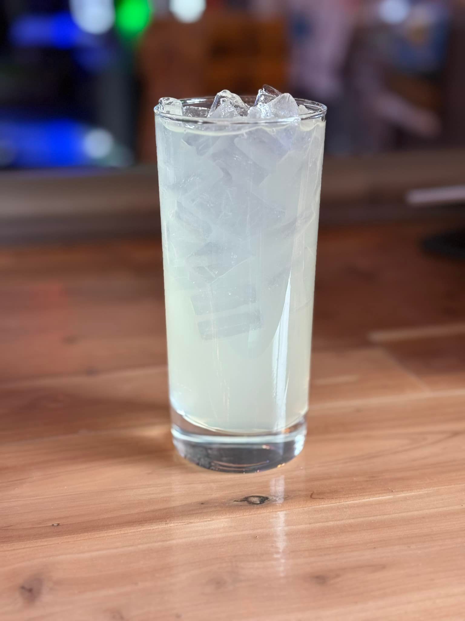 A glass of lemonade with ice on a wooden table.