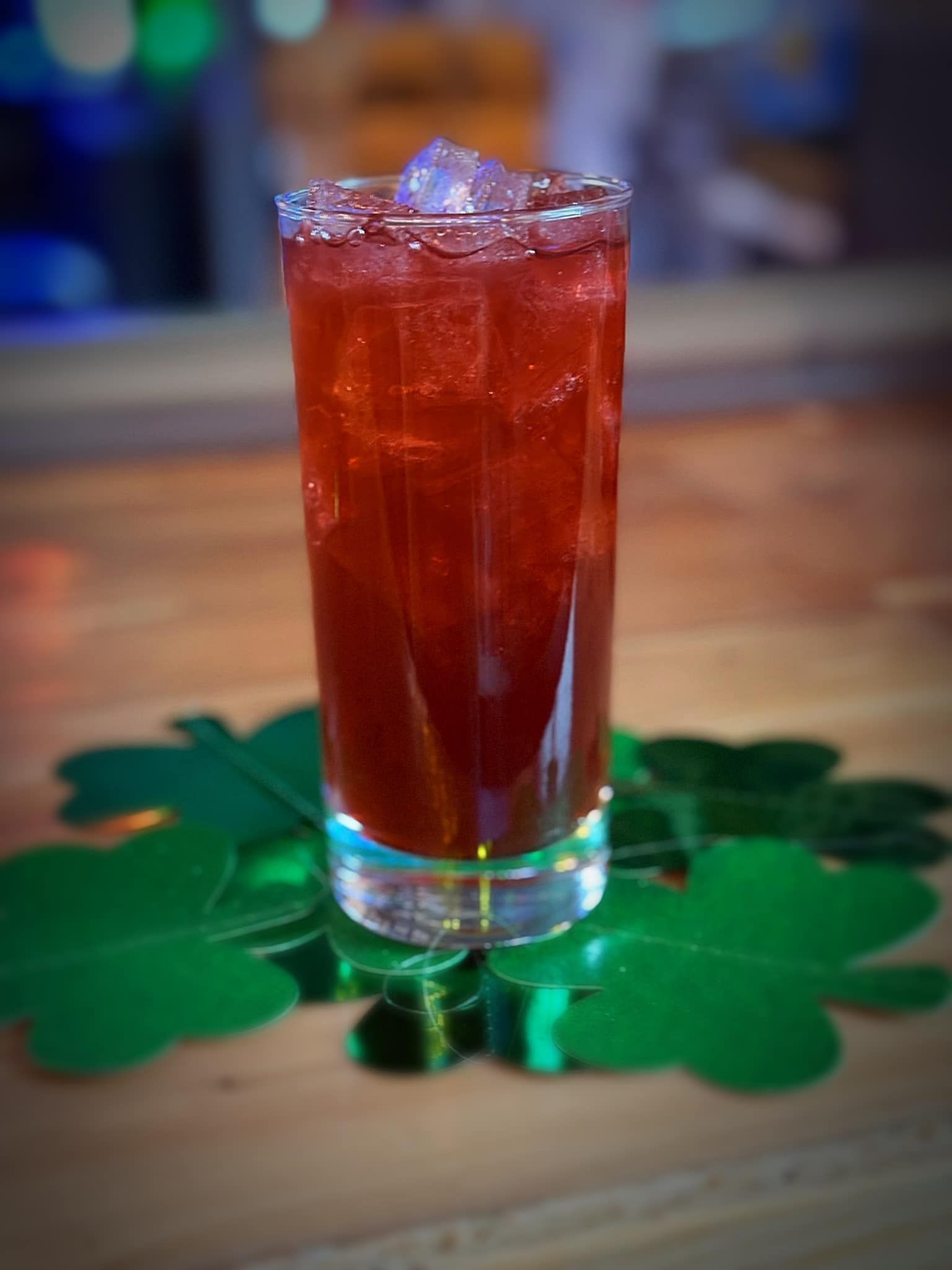 A glass of red liquid is sitting on top of a green shamrock on a table.