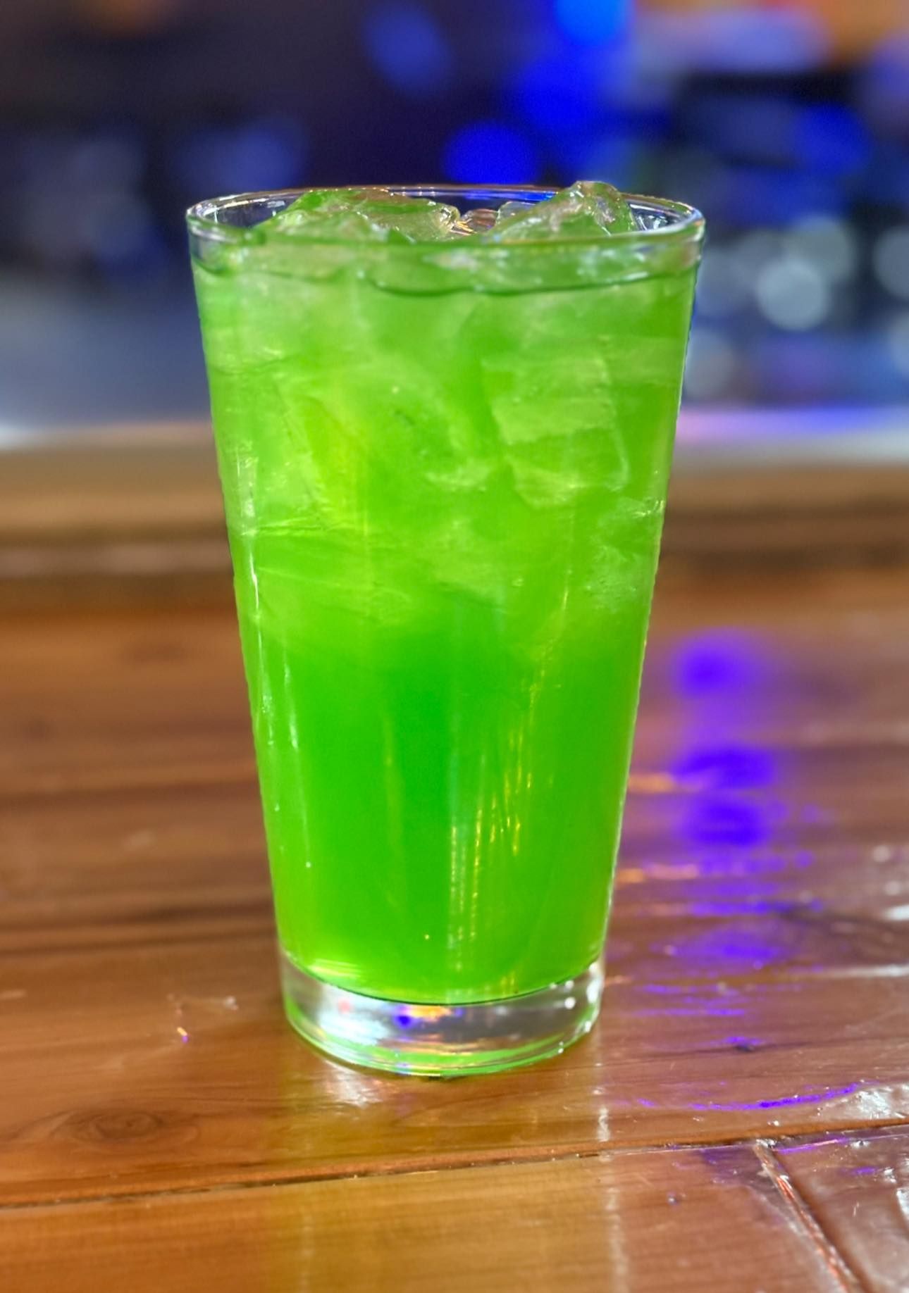 A glass of green liquid is sitting on a wooden table.