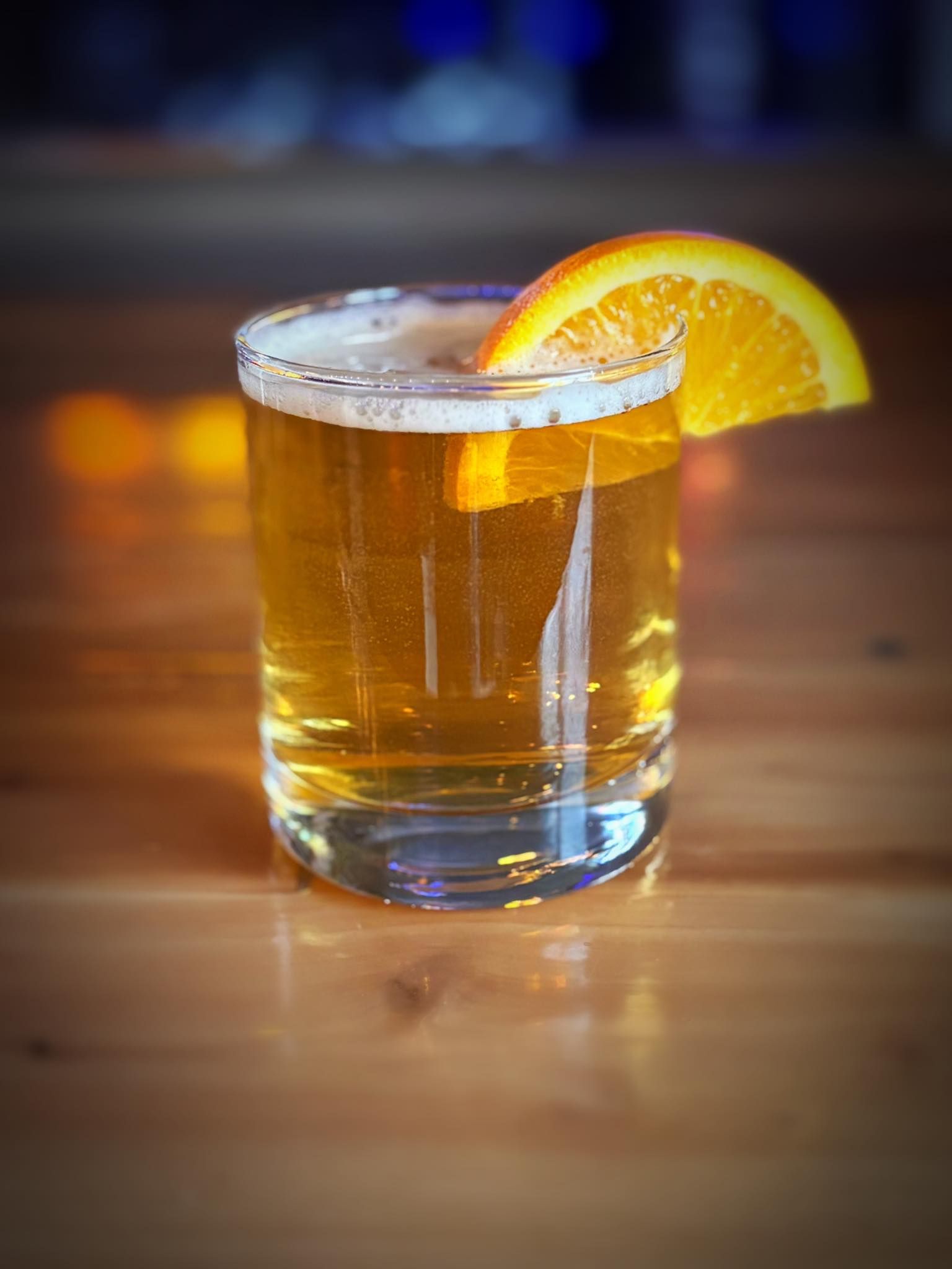 A glass of beer with an orange slice on a wooden table.