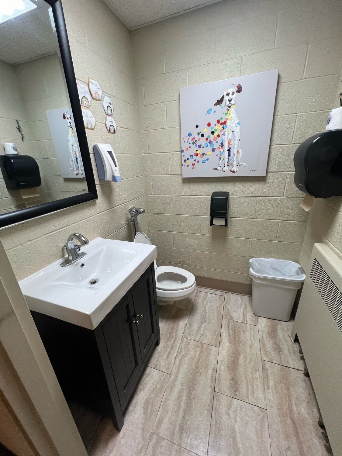 A bathroom with a sink, toilet, and a dog painting on the wall.