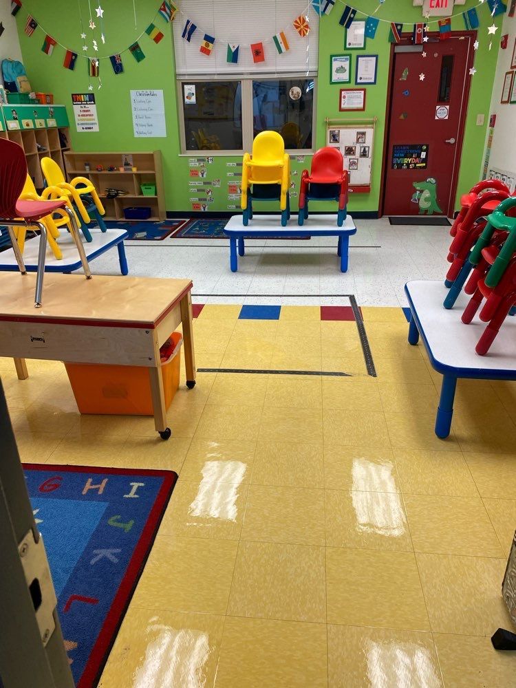 A classroom with tables and chairs and a rug with the letter H on it.
