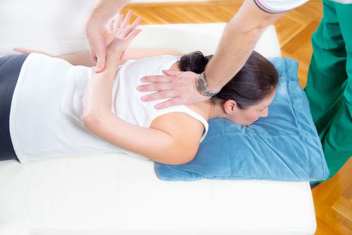 Physical therapist assisting a patient lying face down on a treatment table during a back massage