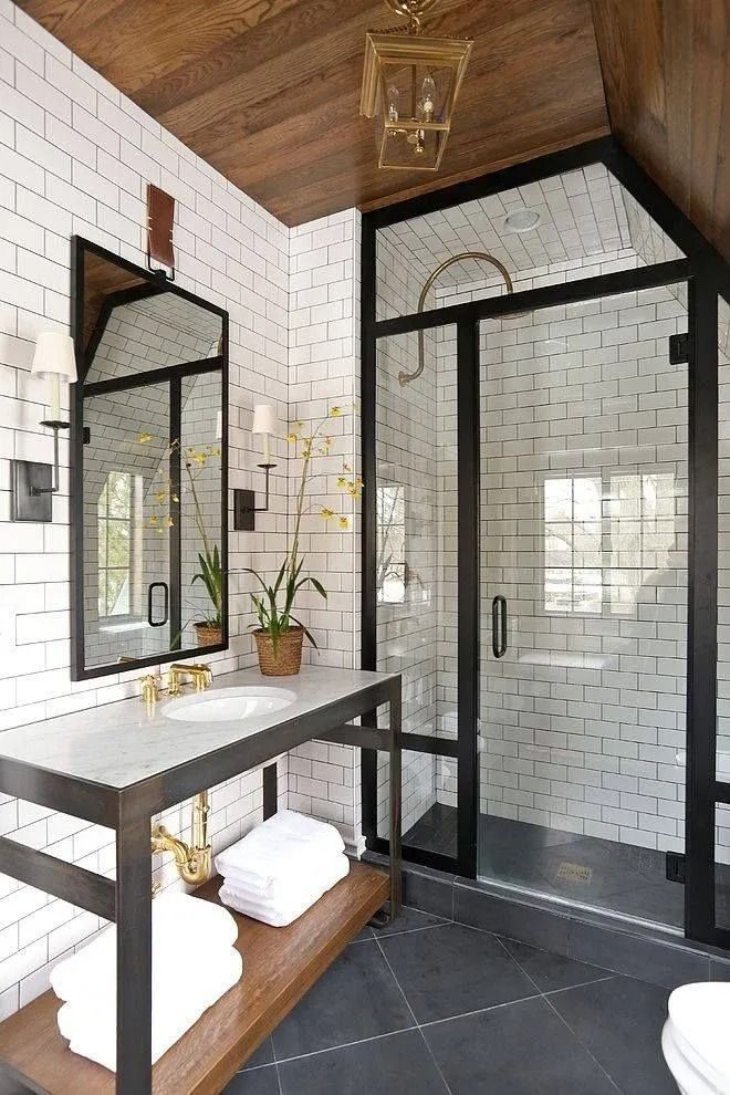 Bathroom with white subway tile, black framed shower and mirror, dark wood accents.