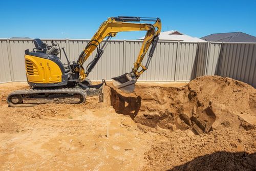 Yellow excavator digging sand in a construction site beside a metal fence.