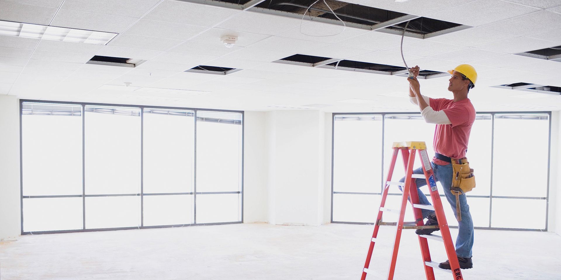 Electrician standing on a ladder working on a ceiling.