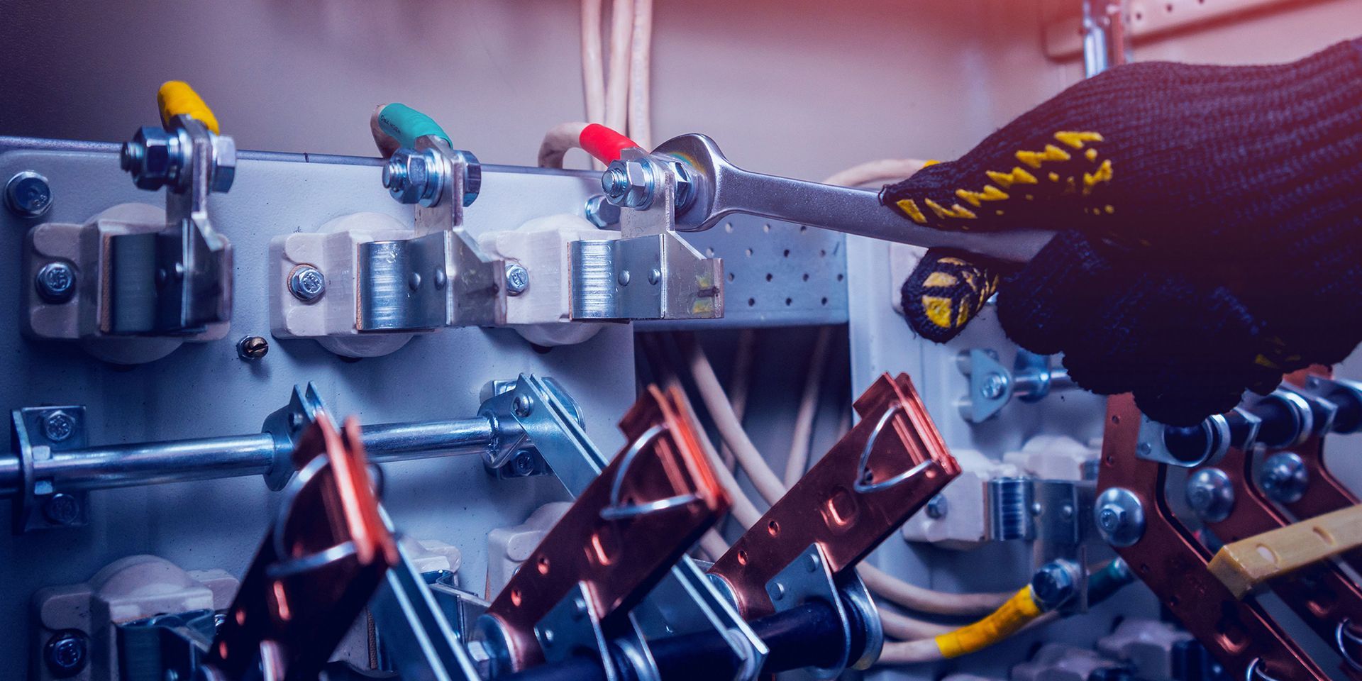 An electrician is working on an electrical box with a wrench.