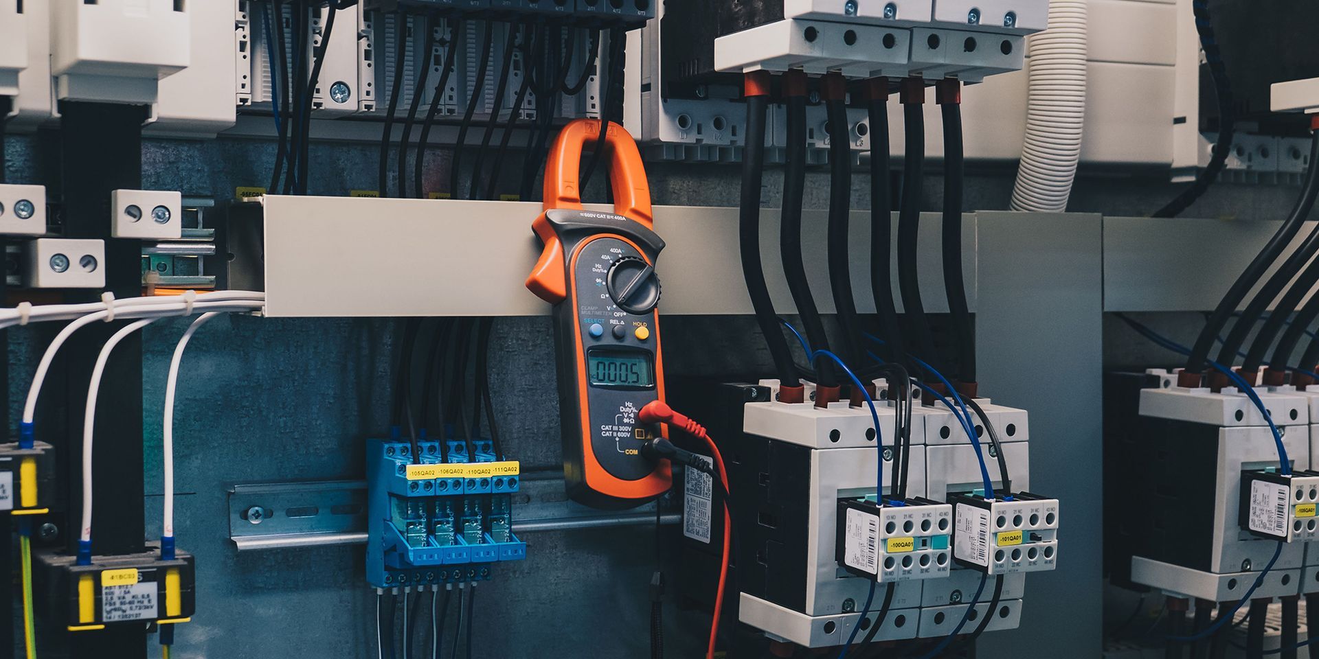 A close up of an electrical panel with a clamp meter on it.