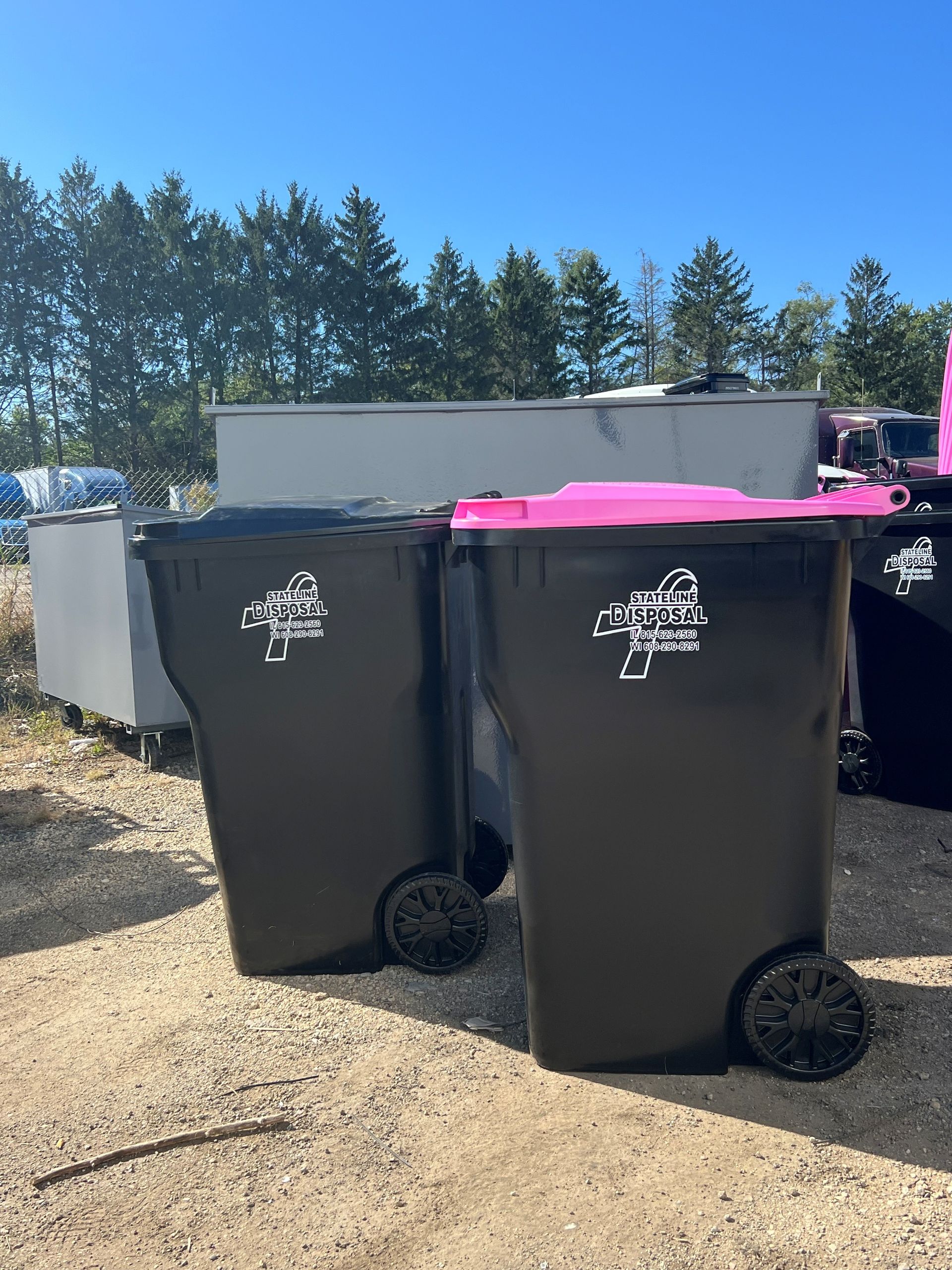 Two black garbage cans with pink lids are sitting on a gravel road