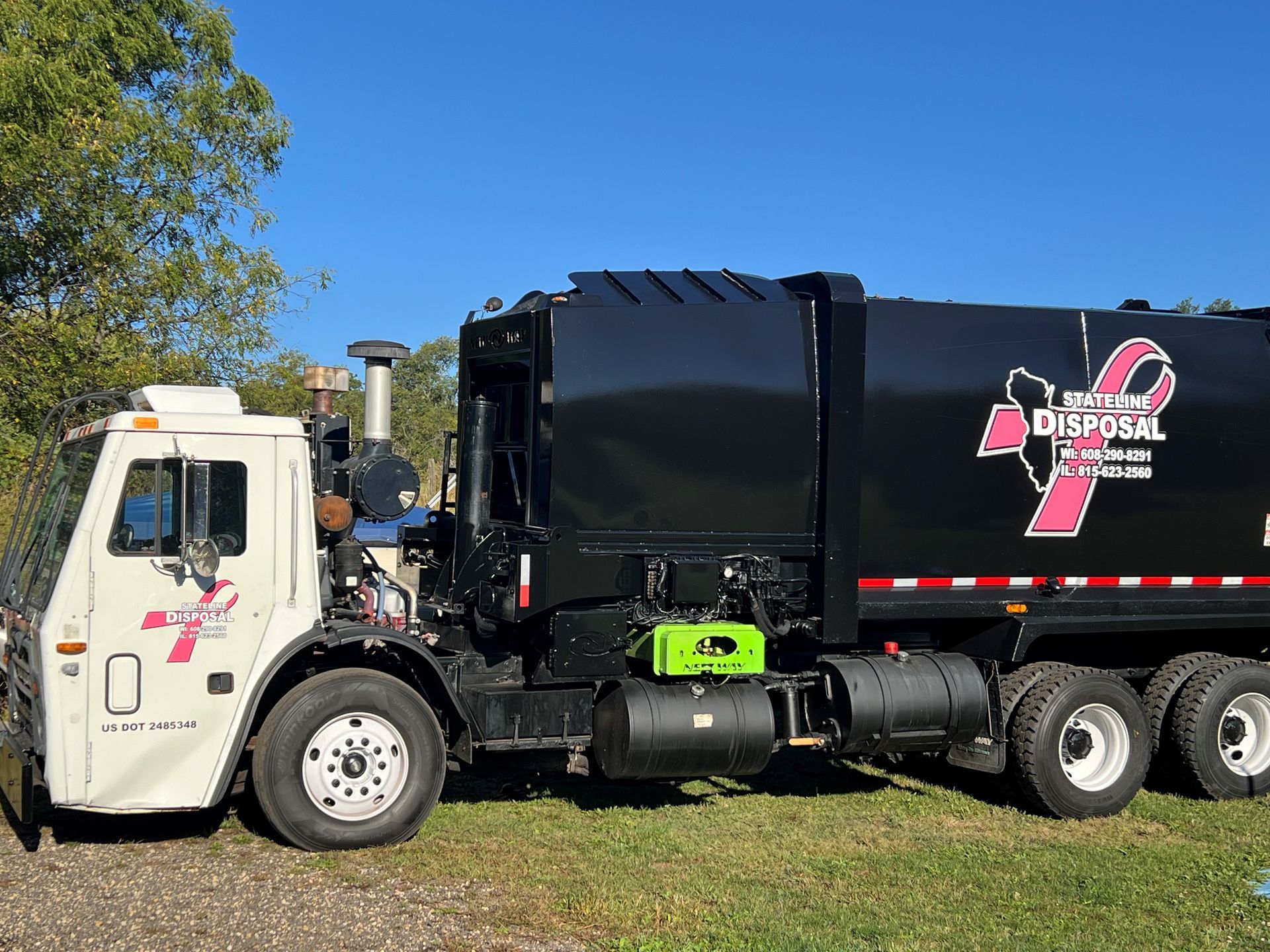 A white garbage truck is parked next to a black garbage truck