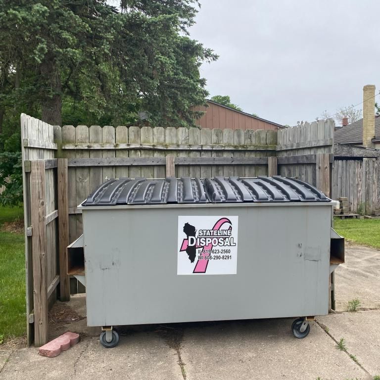 a dumpster with a pink ribbon on it is sitting in front of a wooden fence