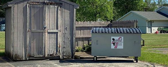 a dumpster is parked next to a wooden shed