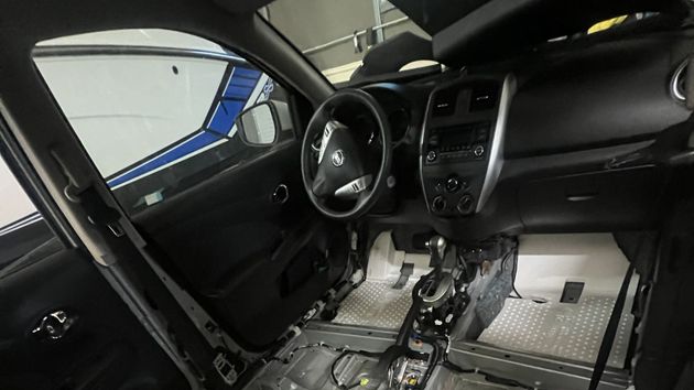 Car interior stripped for repair, showing exposed floor, dashboard, and steering wheel under bright workshop lighting