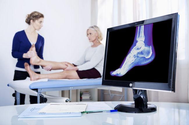 Doctor examining patient's foot; x-ray visible on monitor.