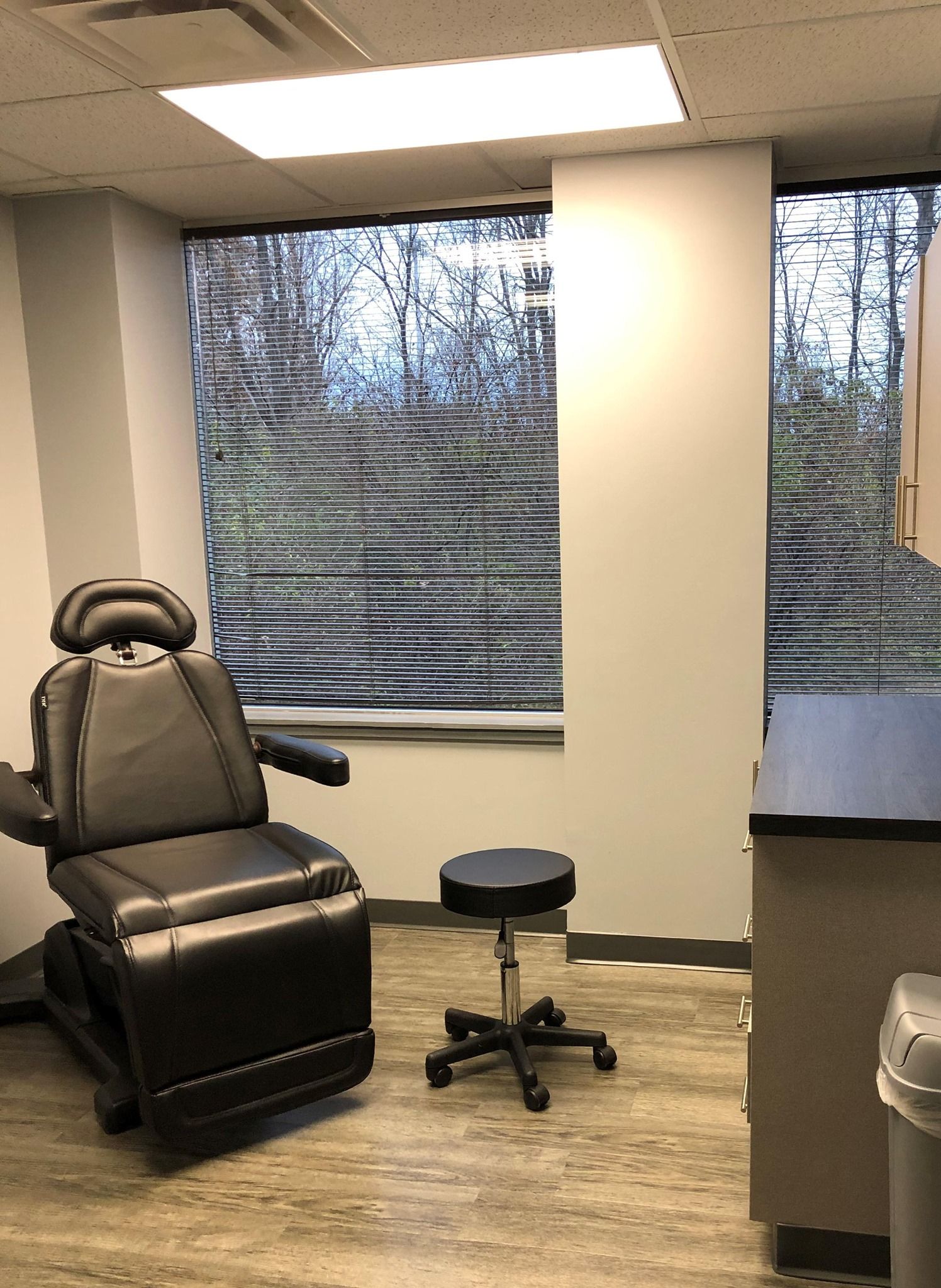 Examination room with a black chair, stool, and window.
