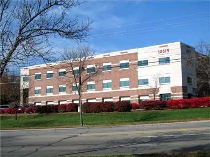 Multi-story office building with brick and white facade, red bushes, and green grass. Number 10615 on top.