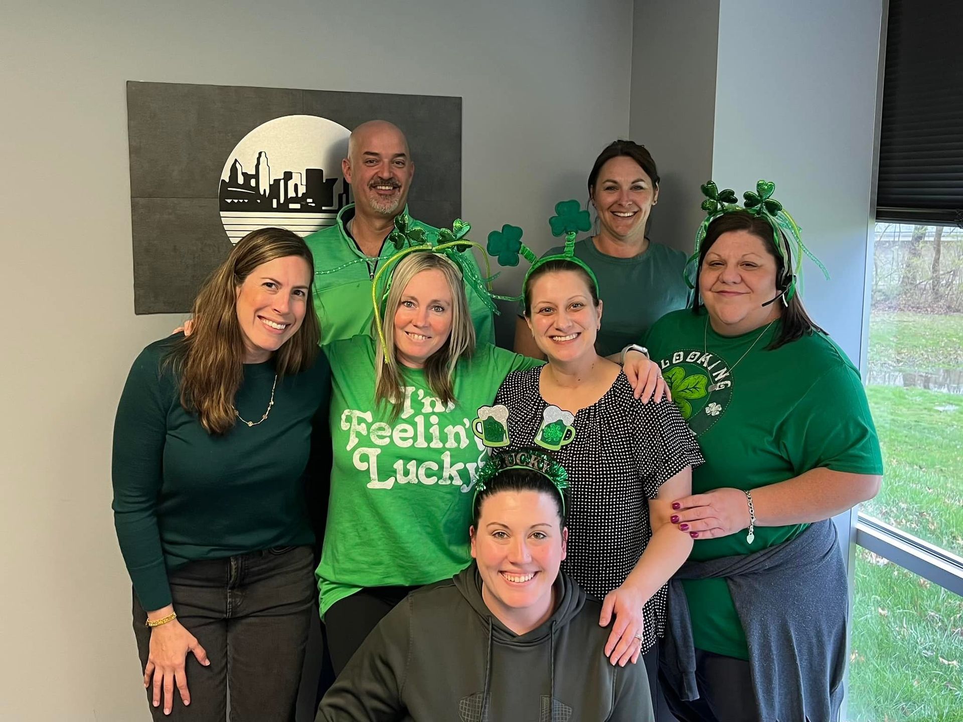 Group of people wearing green, celebrating St. Patrick's Day. They are in an office setting.