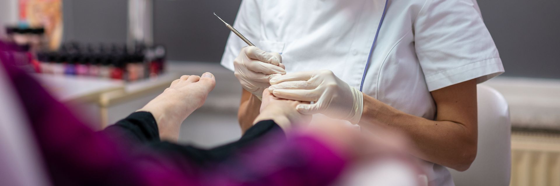 Manicurist working on a client's foot in a salon, using tools and wearing gloves.