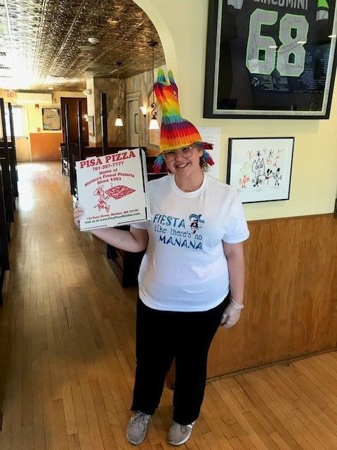 A woman wearing a rainbow hat is holding a pizza box