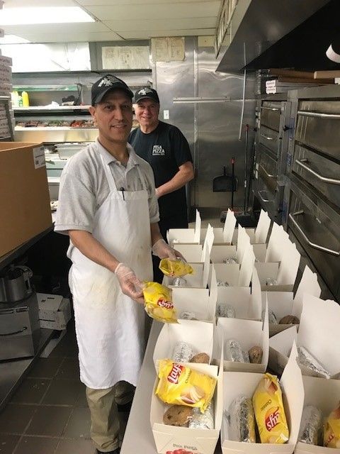 Two men are standing in a kitchen holding bags of lays chips
