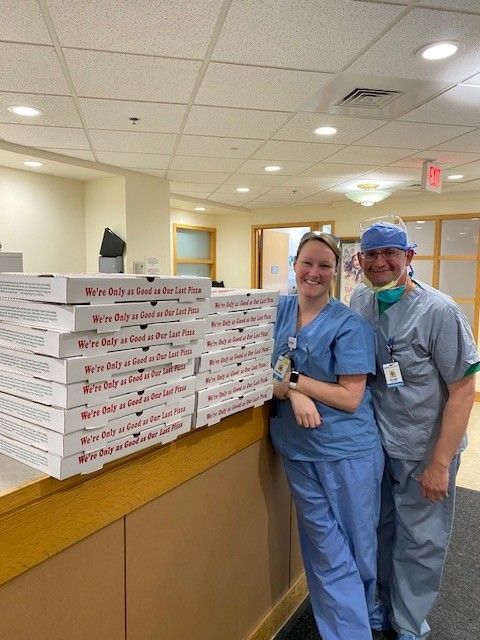 A man and a woman are standing next to a stack of pizza boxes.